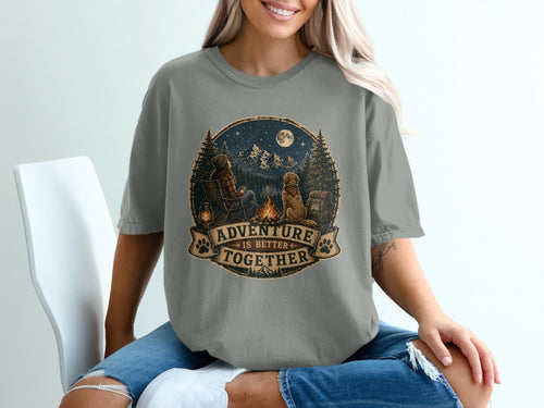 Graphic t-shirt with woman and dog by campfire, reads "Adventure is Better Together".