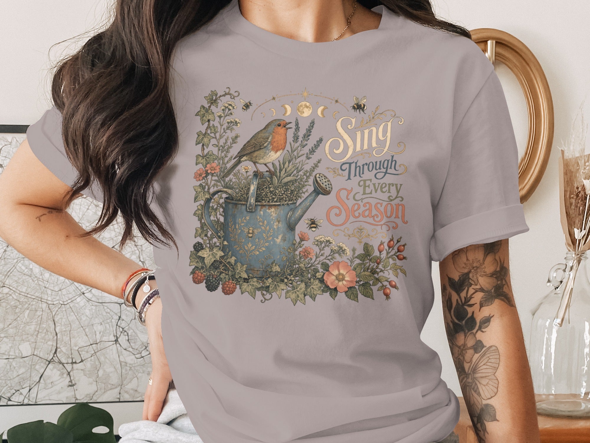 Robin on watering can with flowers and bees; text "Sing Through Every Season".