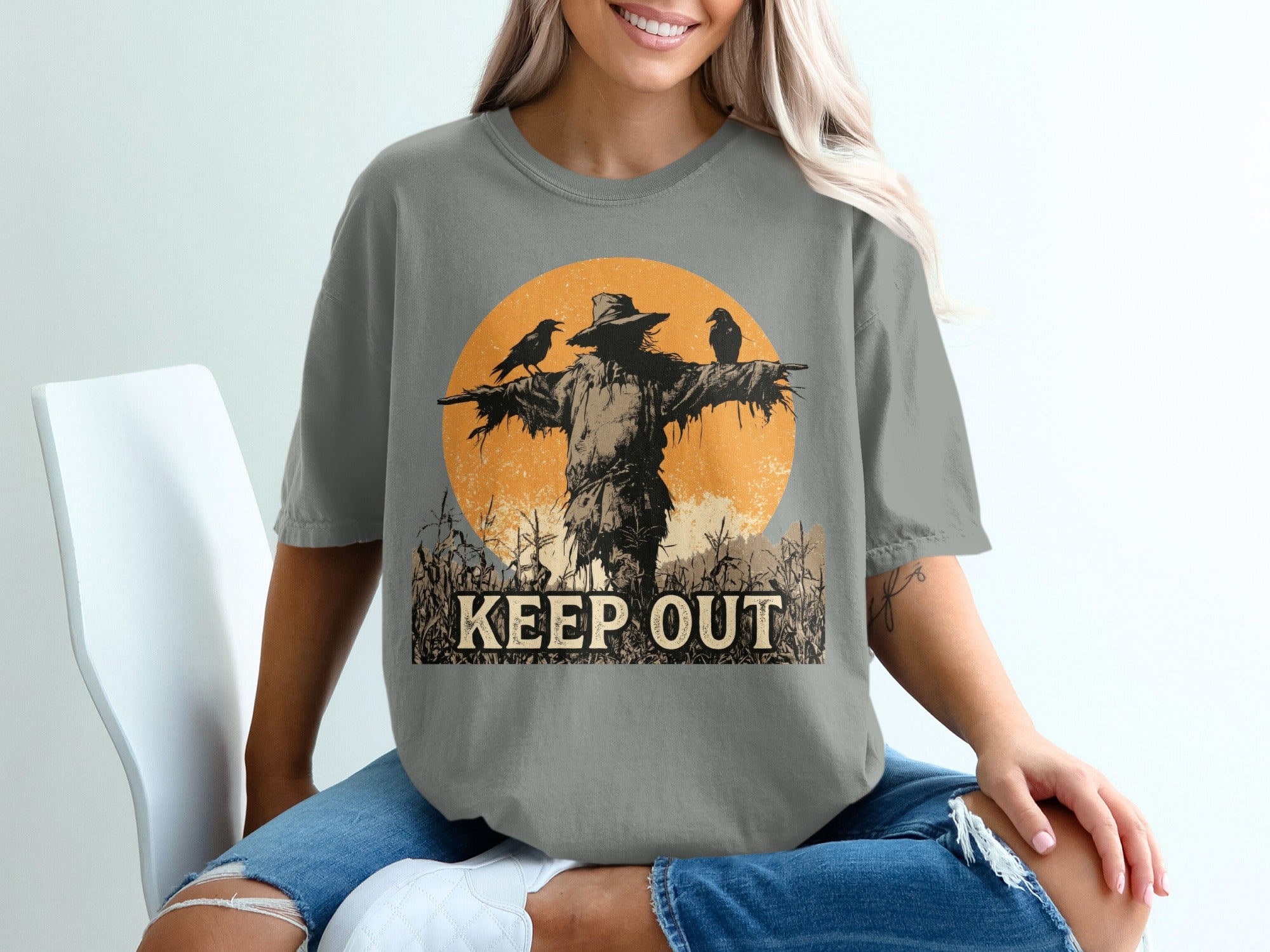 Scarecrow with crows and "KEEP OUT" text against a textured orange circle.