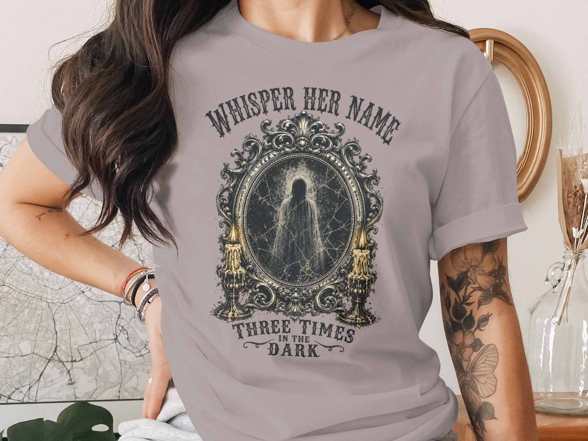 T-shirt with framed ghostly figure, candles and text: "Whisper her name three times in the dark."