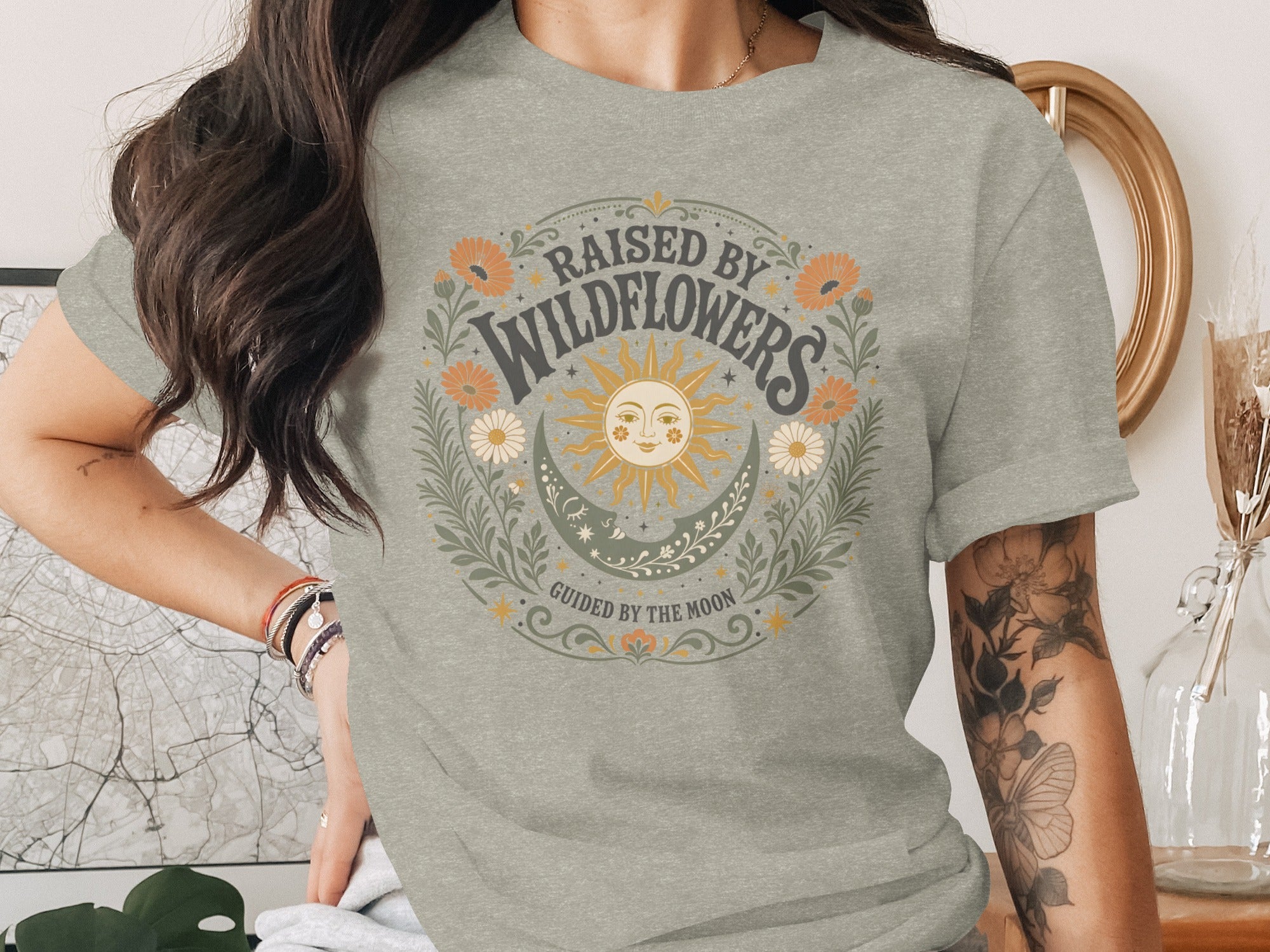 Light gray t-shirt with "RAISED BY WILDFLOWERS GUIDED BY THE MOON" graphic.
