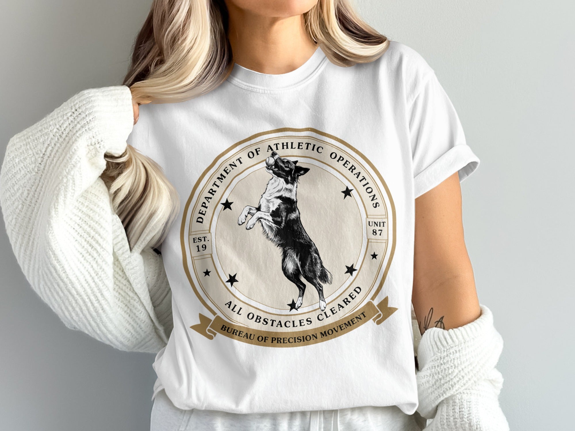White t-shirt with a round graphic featuring a black and white dog, "Department of Athletic Operations," and "All Obstacles Cleared."