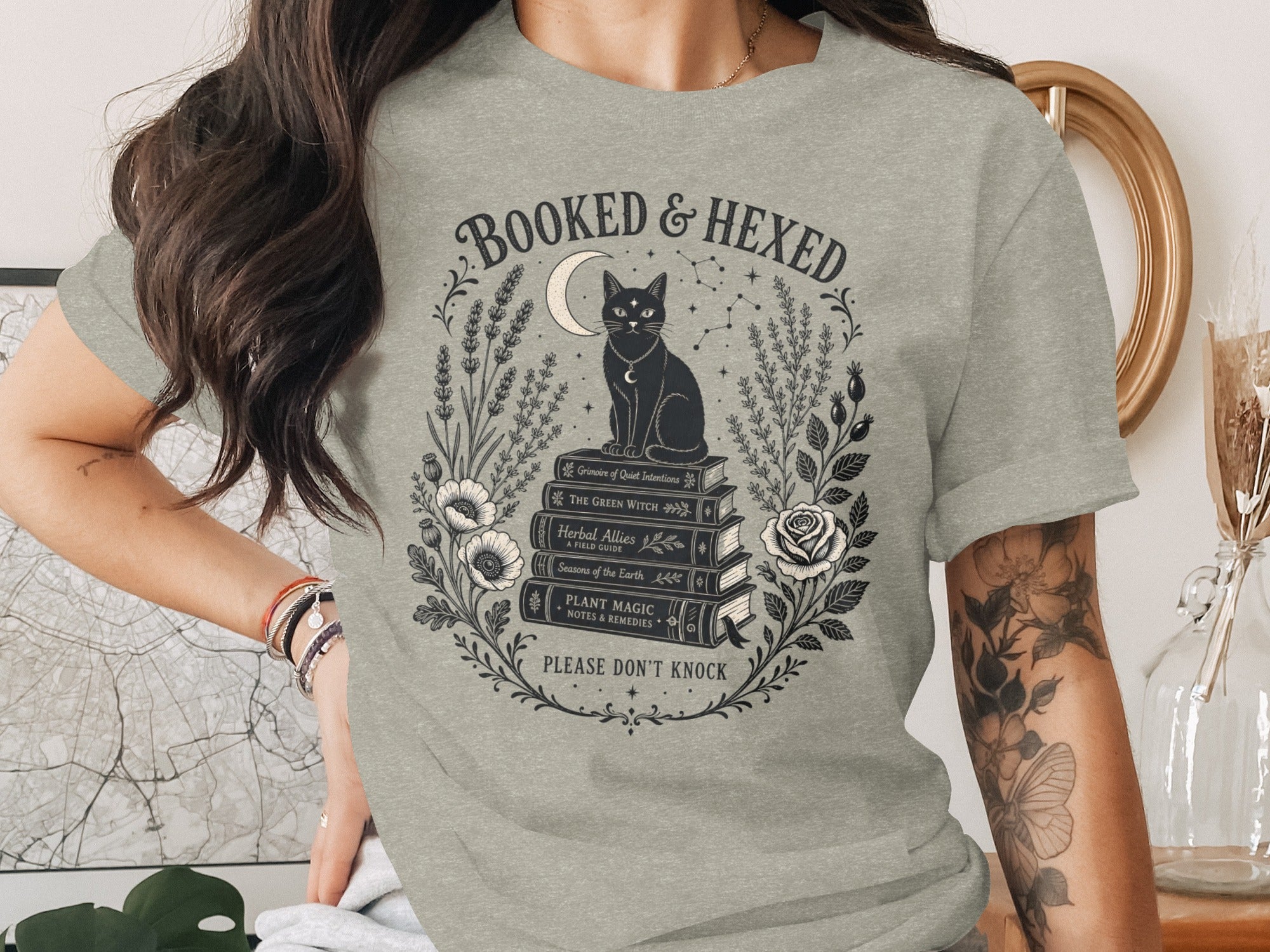 T-shirt graphic: black cat on books with moon and text "BOOKED & HEXED".