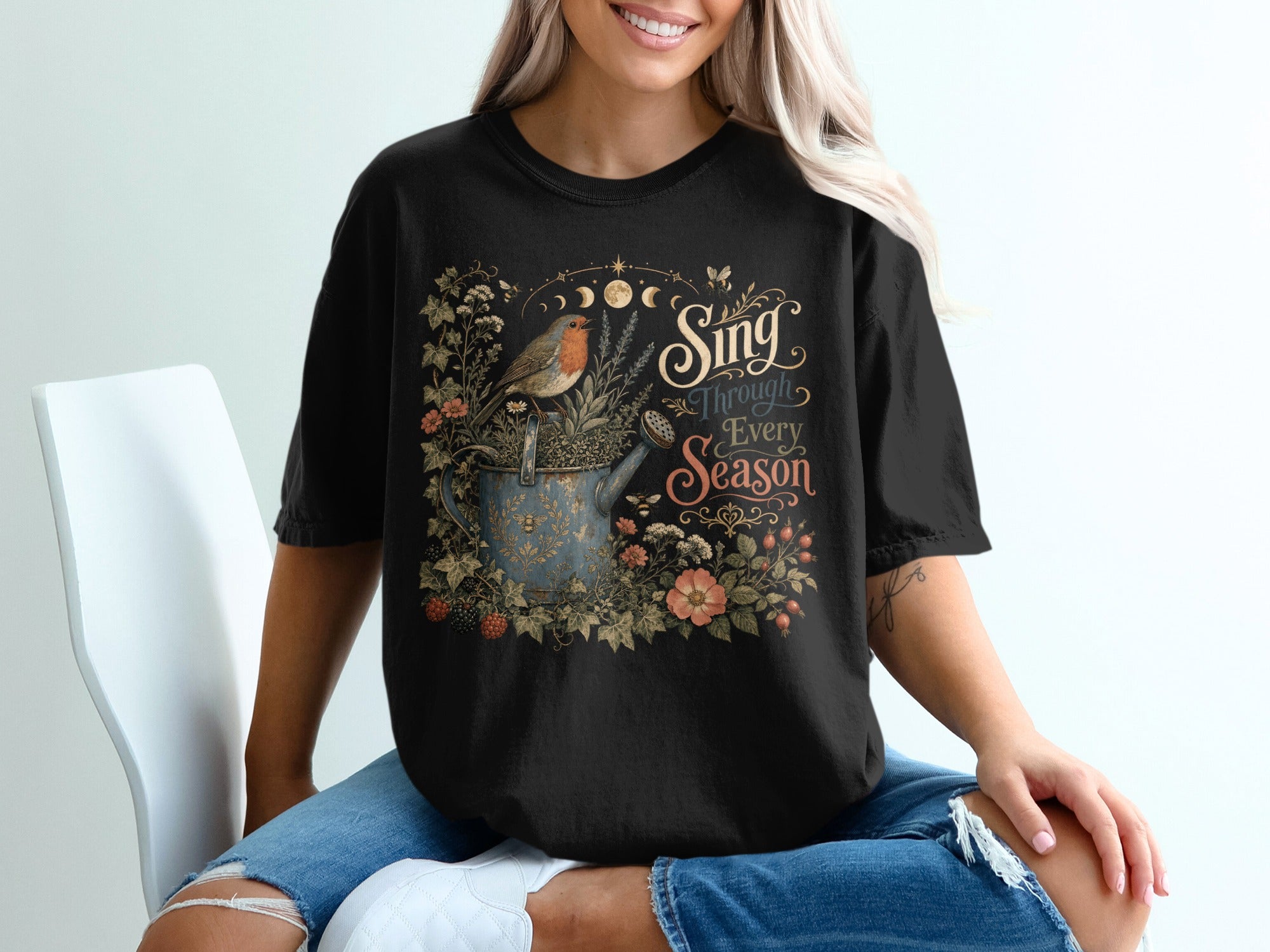Black t-shirt with "Sing Through Every Season" text and a robin on a watering can.