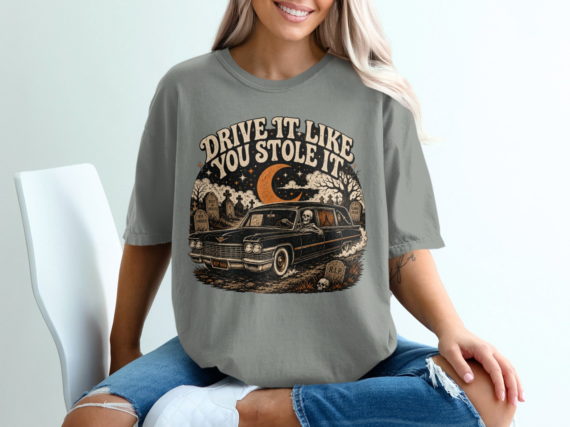 T-shirt graphic of skeleton driving a hearse through a graveyard with text.