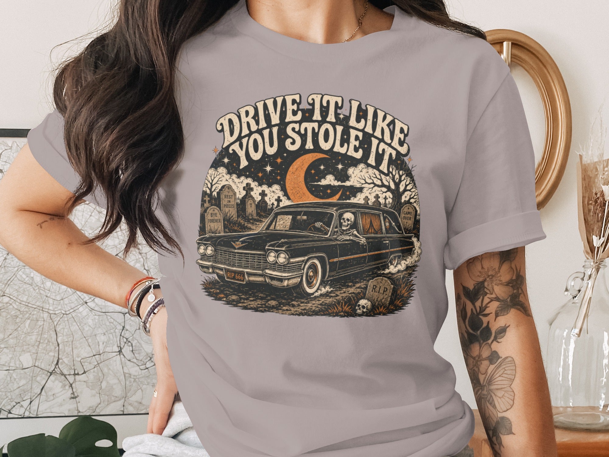 Skeleton driving a classic car through a graveyard with text "DRIVE IT LIKE YOU STOLE IT."