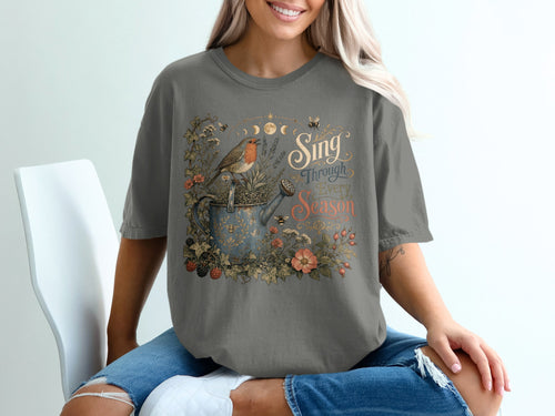 T-shirt graphic of a bird on a watering can with floral and bee illustrations and text.