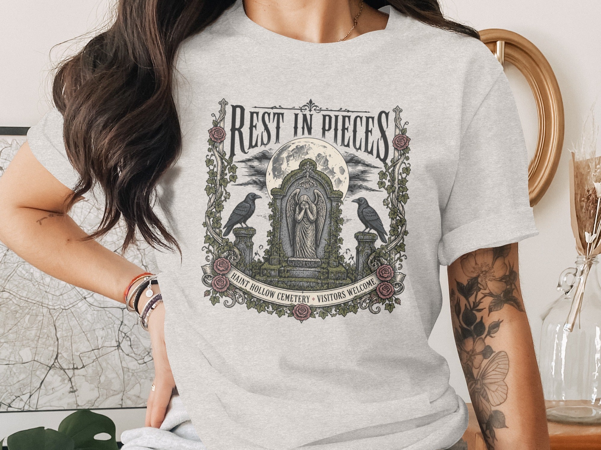 T-shirt graphic: "Rest in Pieces" over a cemetery scene with crows and full moon.