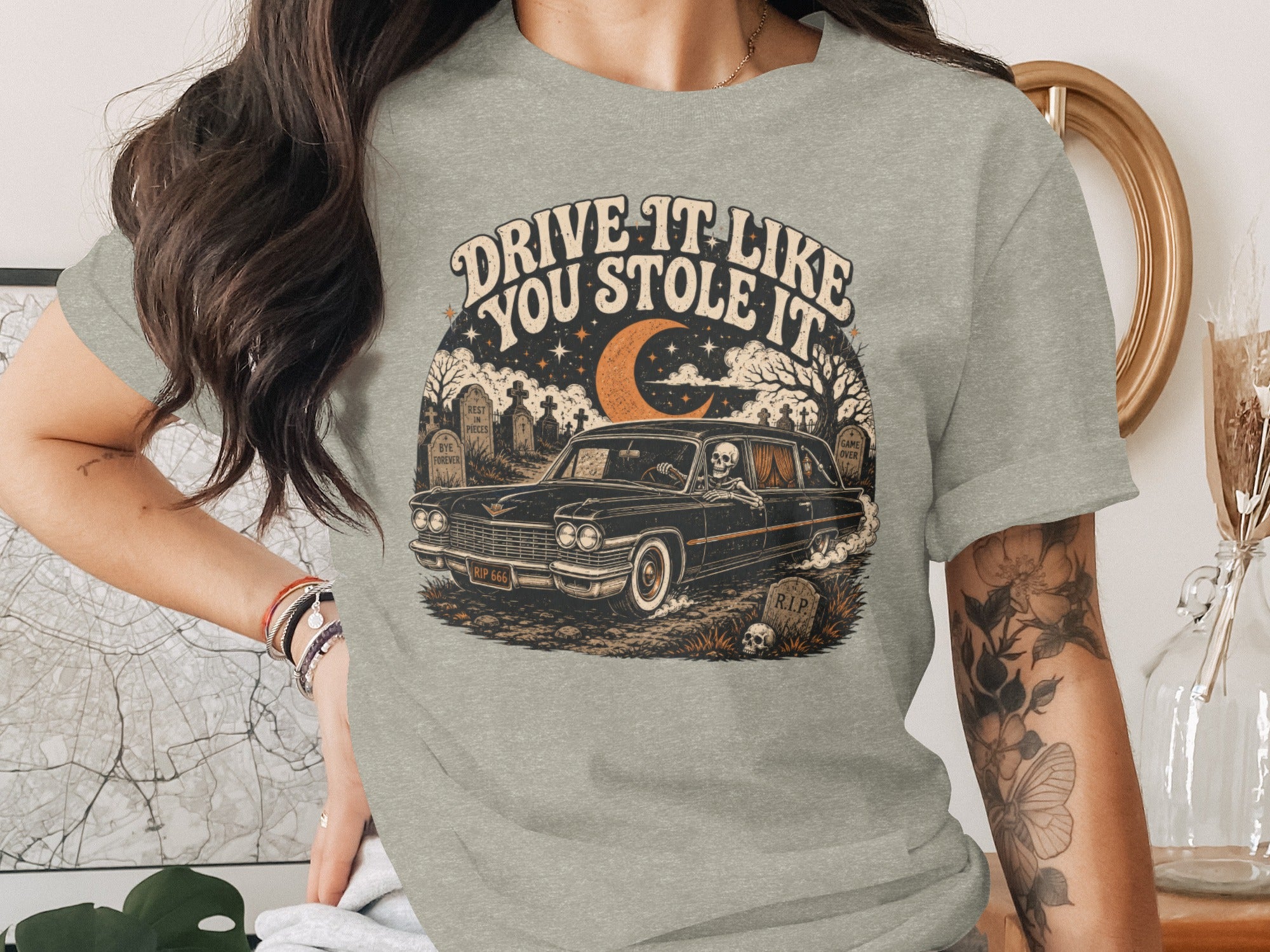 T-shirt graphic: Skeleton driving a vintage car through a graveyard at night.