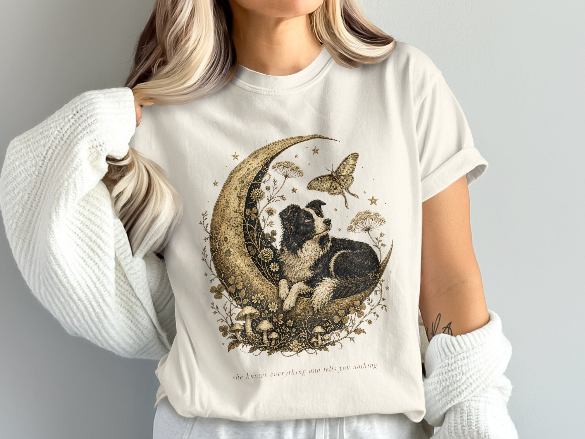 T-shirt graphic: dog on crescent moon with butterfly, mushrooms, and stars. Text: "she knows everything and tells you nothing."