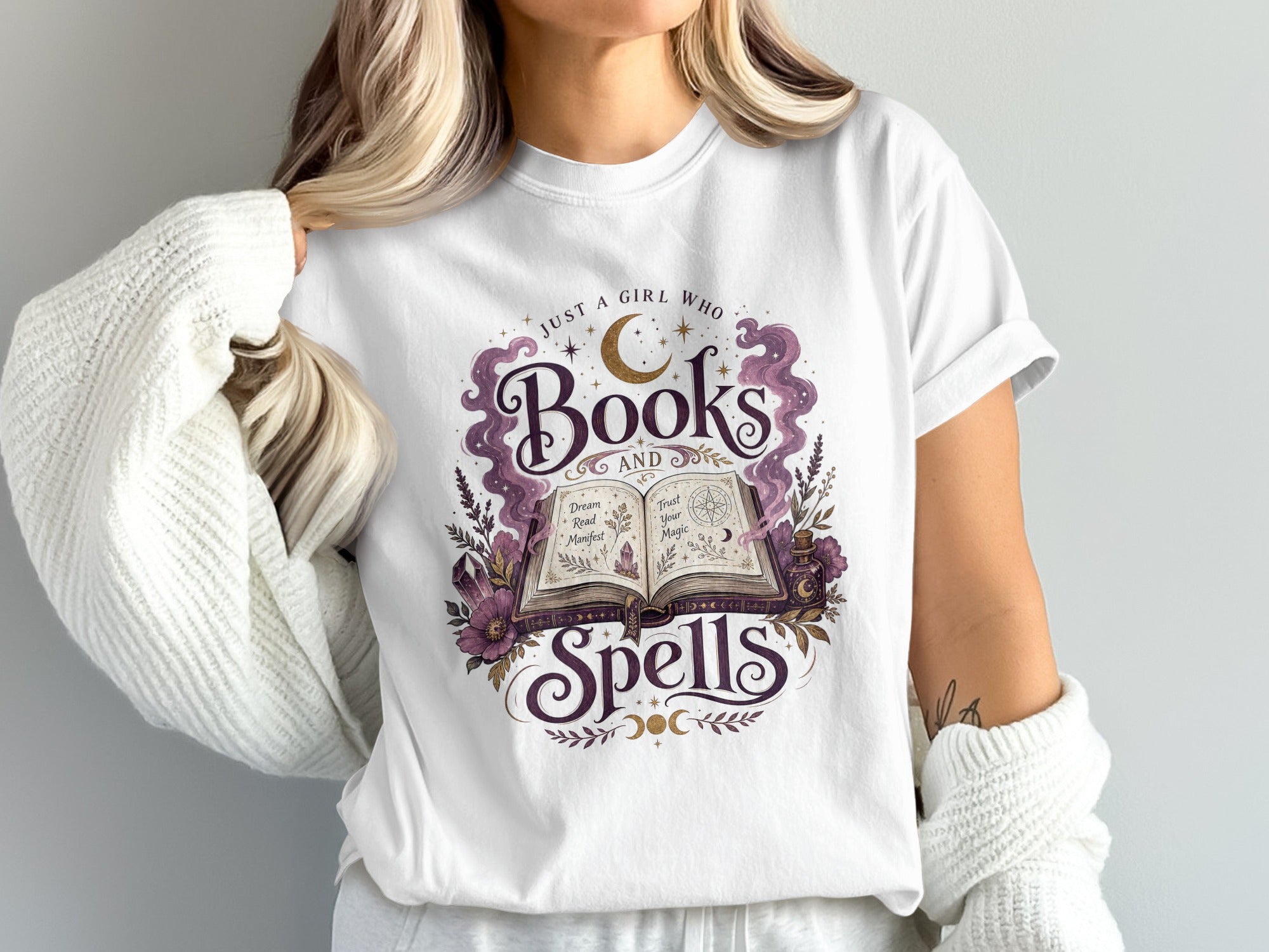 White t-shirt with "Just a girl who books and spells" graphic and open book.