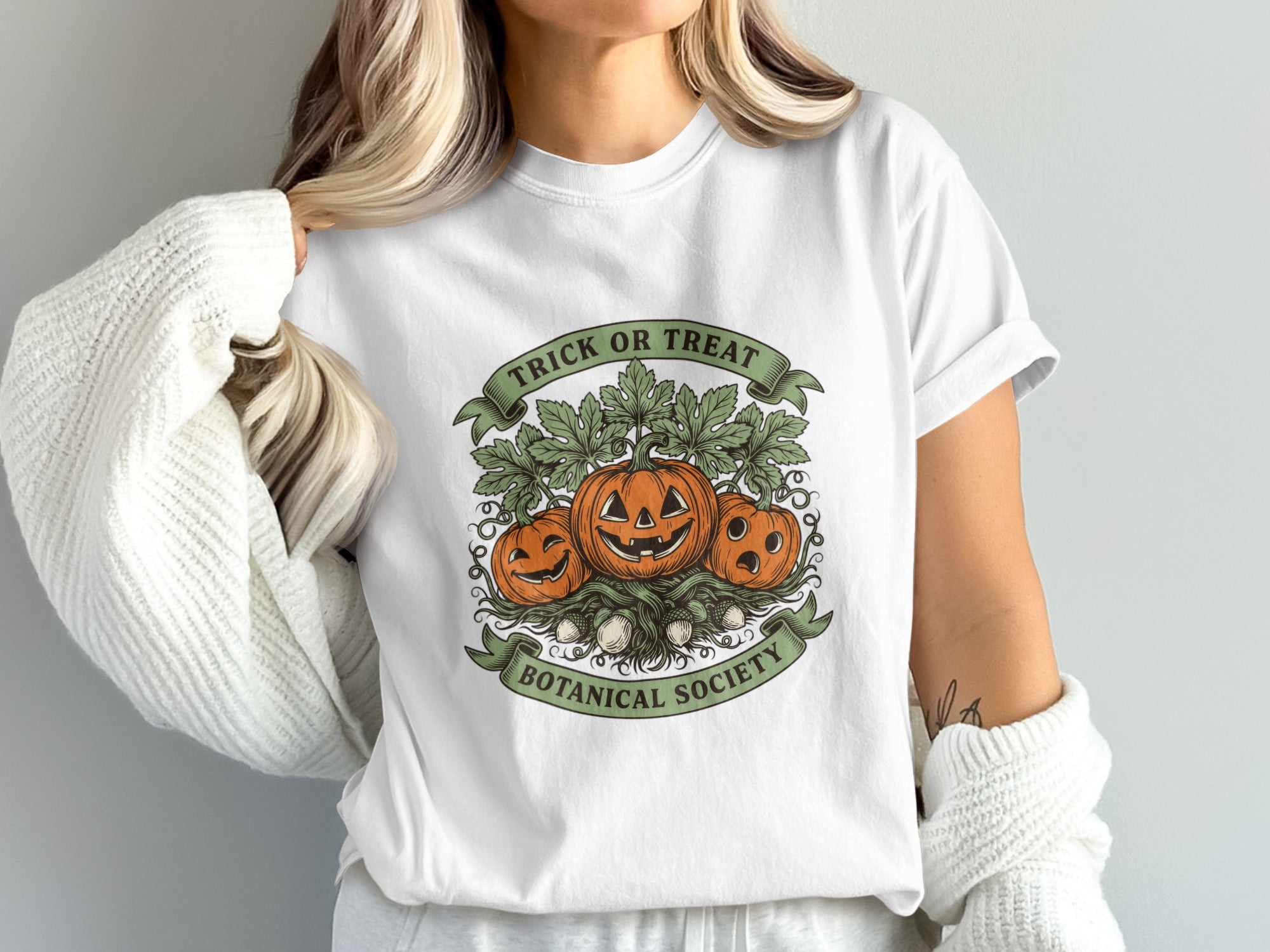 White t-shirt with a graphic of three jack-o'-lanterns and leaves, "Trick or Treat Botanical Society".