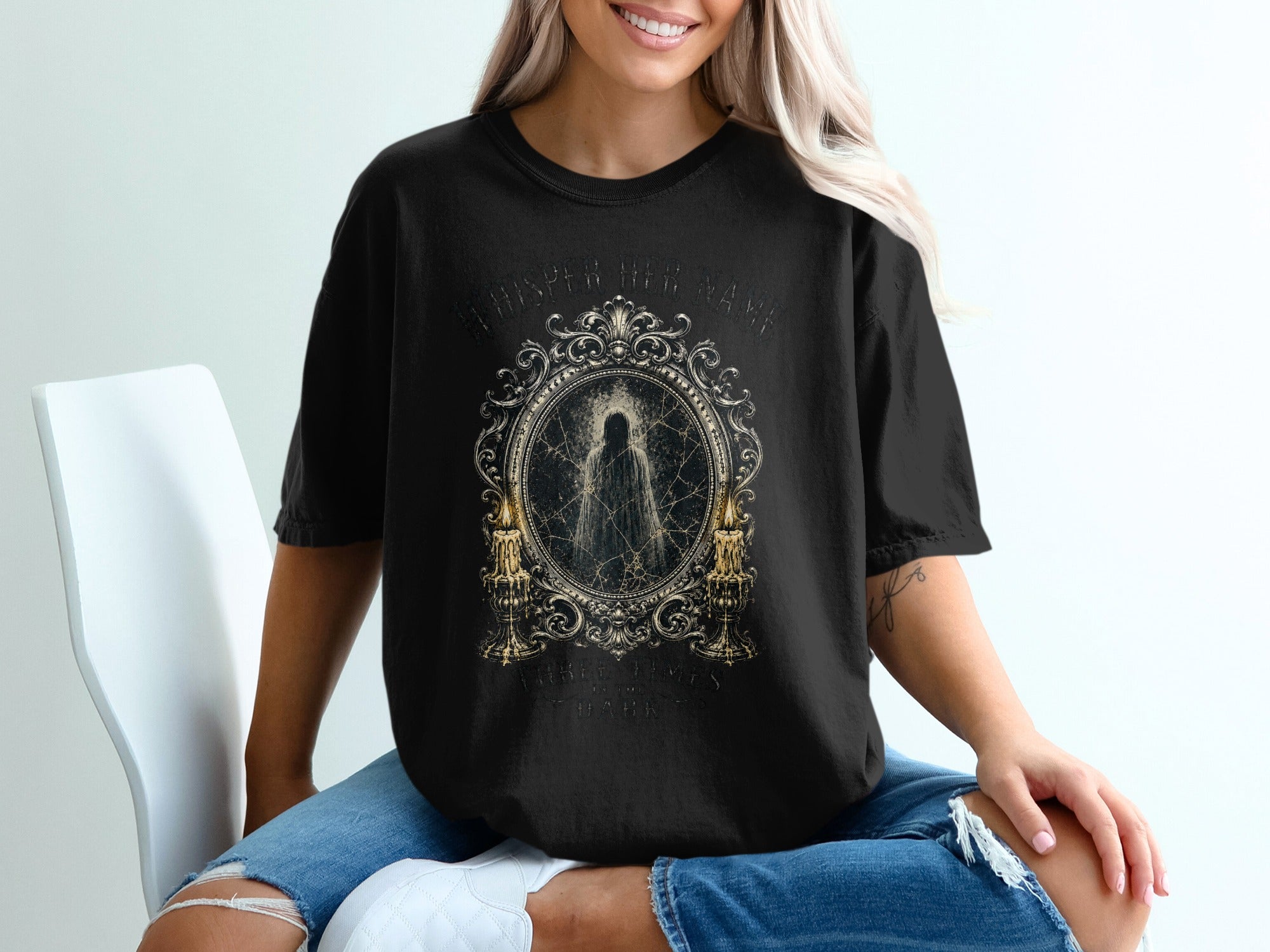 Black t-shirt with ornate frame and "Whisper Her Name" text.