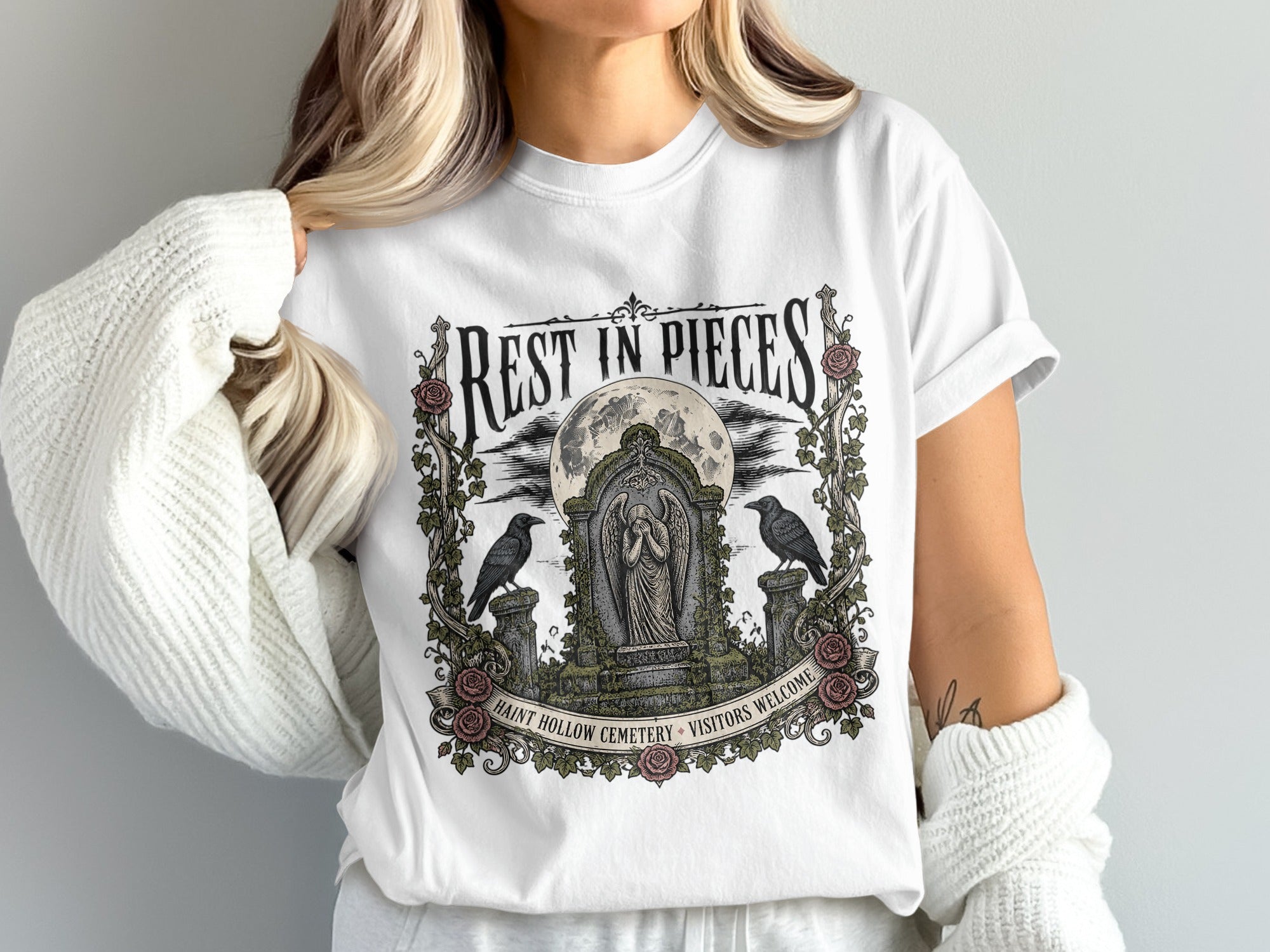 White t-shirt with a "Rest in Pieces" design featuring a cemetery, moon, angels, and crows.