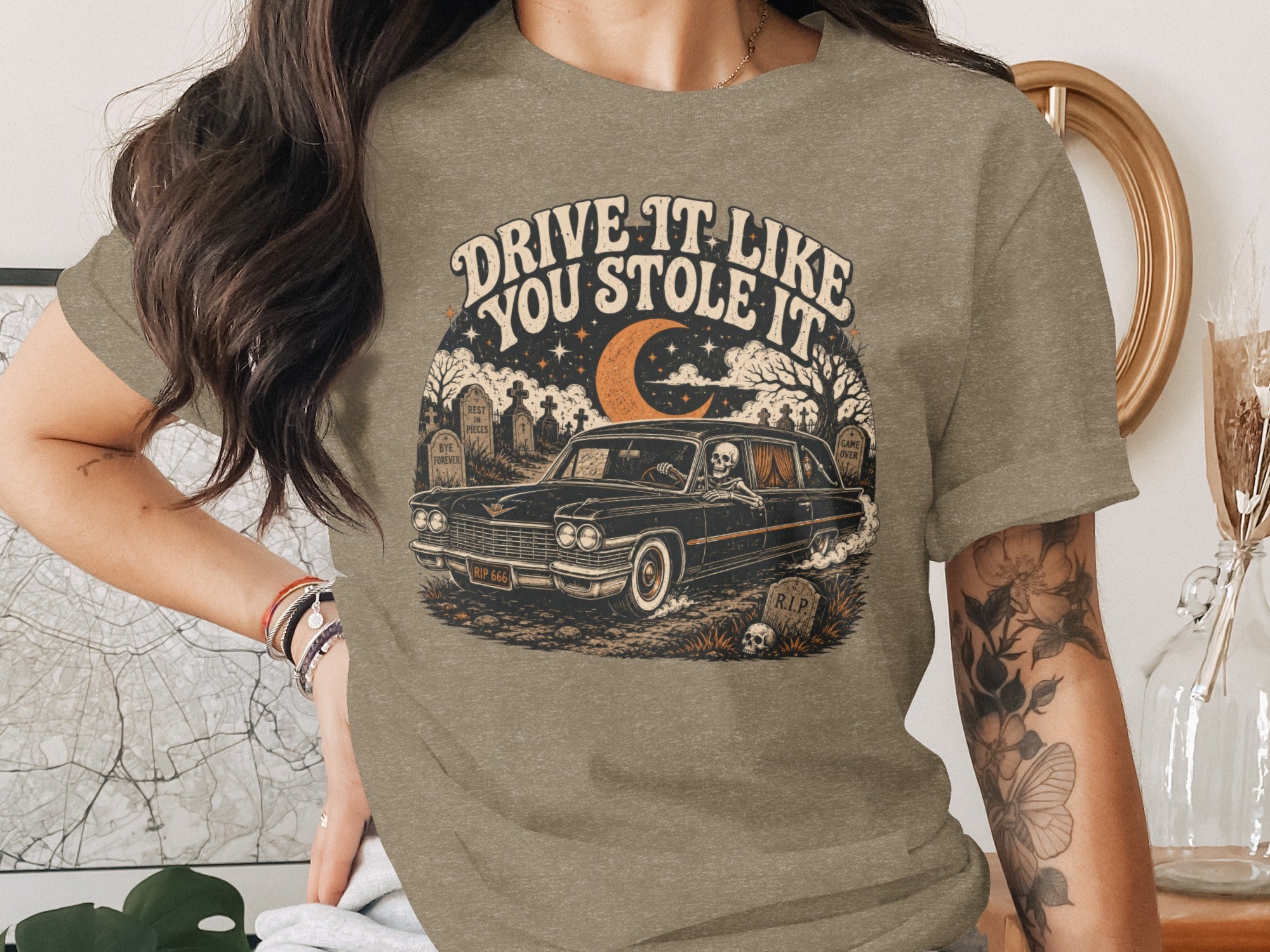 T-shirt with graphic: Skeleton driving hearse through cemetery, "Drive it like you stole it" text.