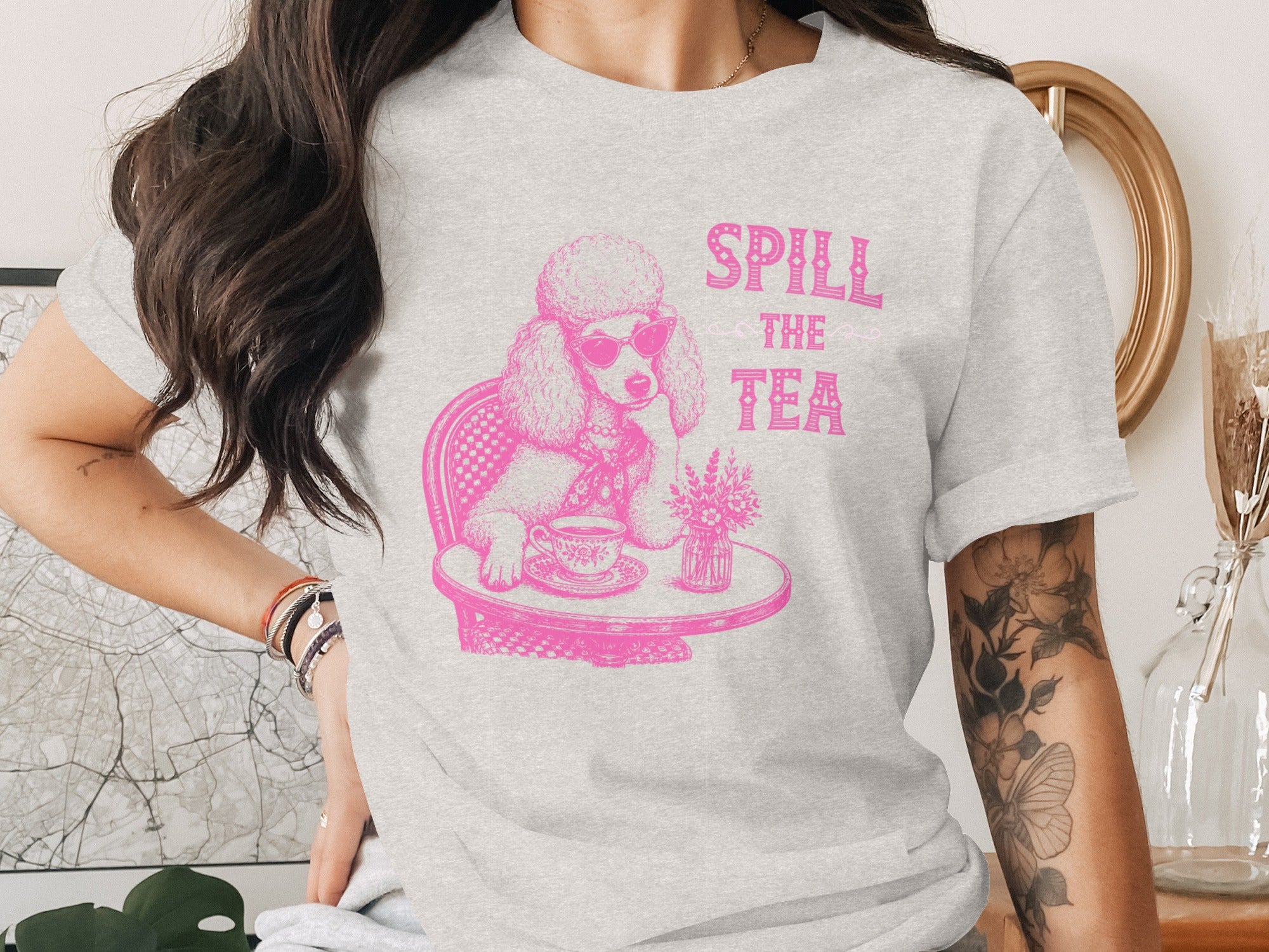Pink poodle in sunglasses sits at a table with tea, text "SPILL THE TEA".