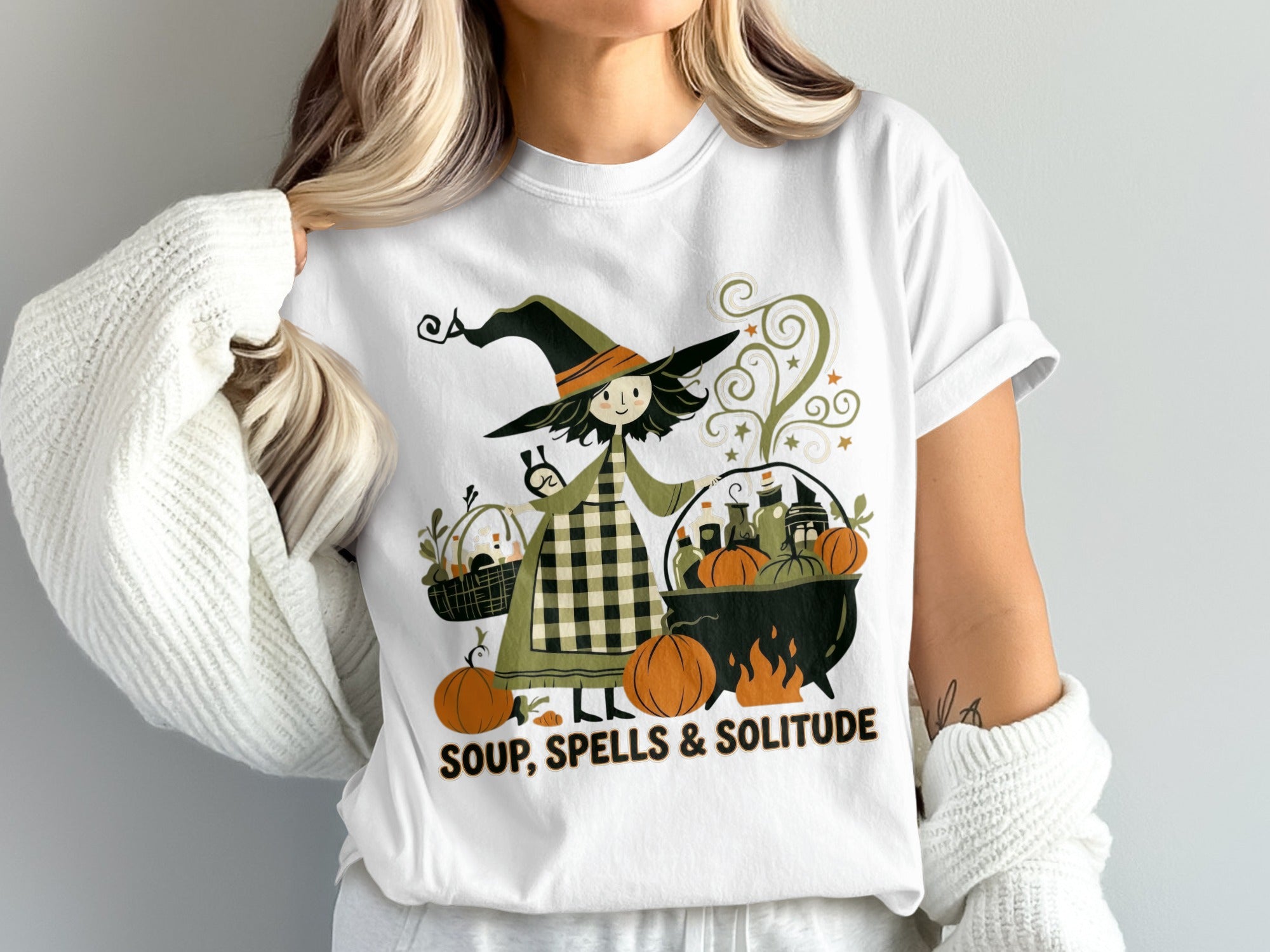 T-shirt graphic of a witch with a cauldron, pumpkins, and the text "SOUP, SPELLS & SOLITUDE".