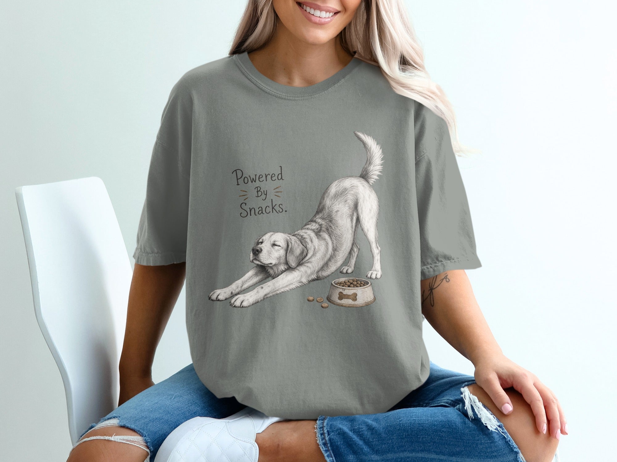 Grey t-shirt with graphic of dog stretching next to food bowl and text "Powered By Snacks."