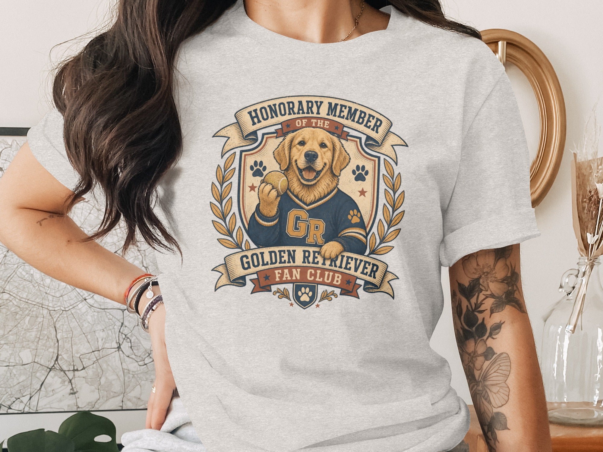 Golden Retriever wearing a jersey holds a tennis ball on a t-shirt graphic.