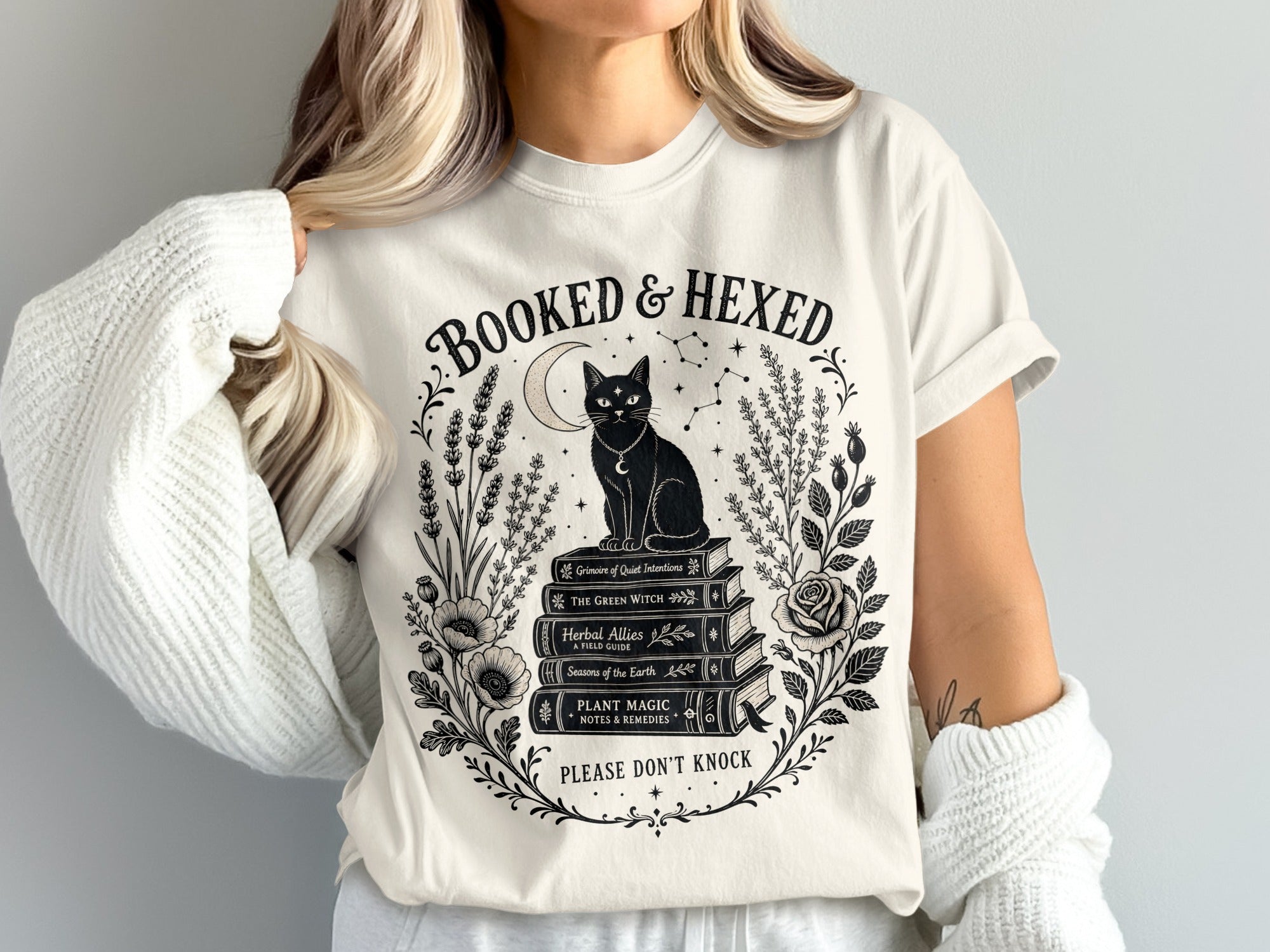 Cream t-shirt with "Booked & Hexed" text, black cat on books, and floral border.