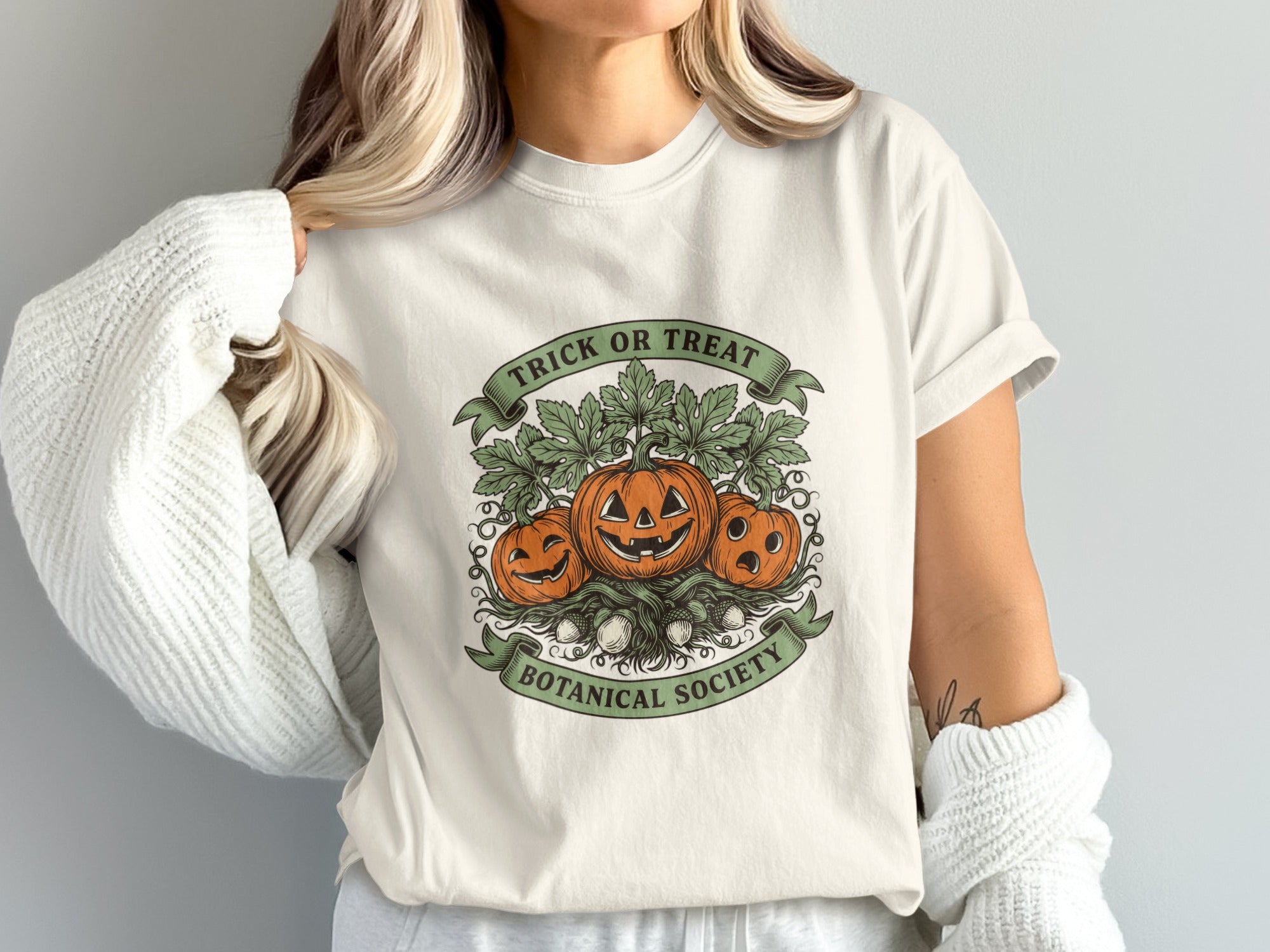 Cream t-shirt with three carved pumpkins, leaves, acorns, and text "TRICK OR TREAT BOTANICAL SOCIETY".