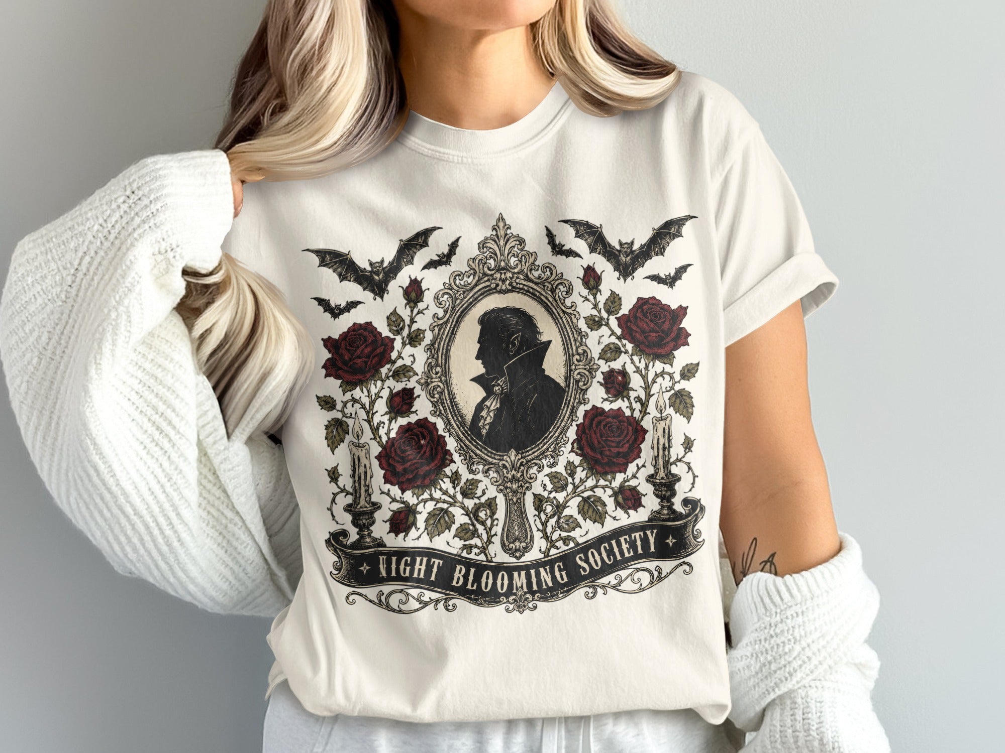 Cream t-shirt with a gothic graphic featuring a vampire silhouette, roses, bats, and the text "Night Blooming Society".