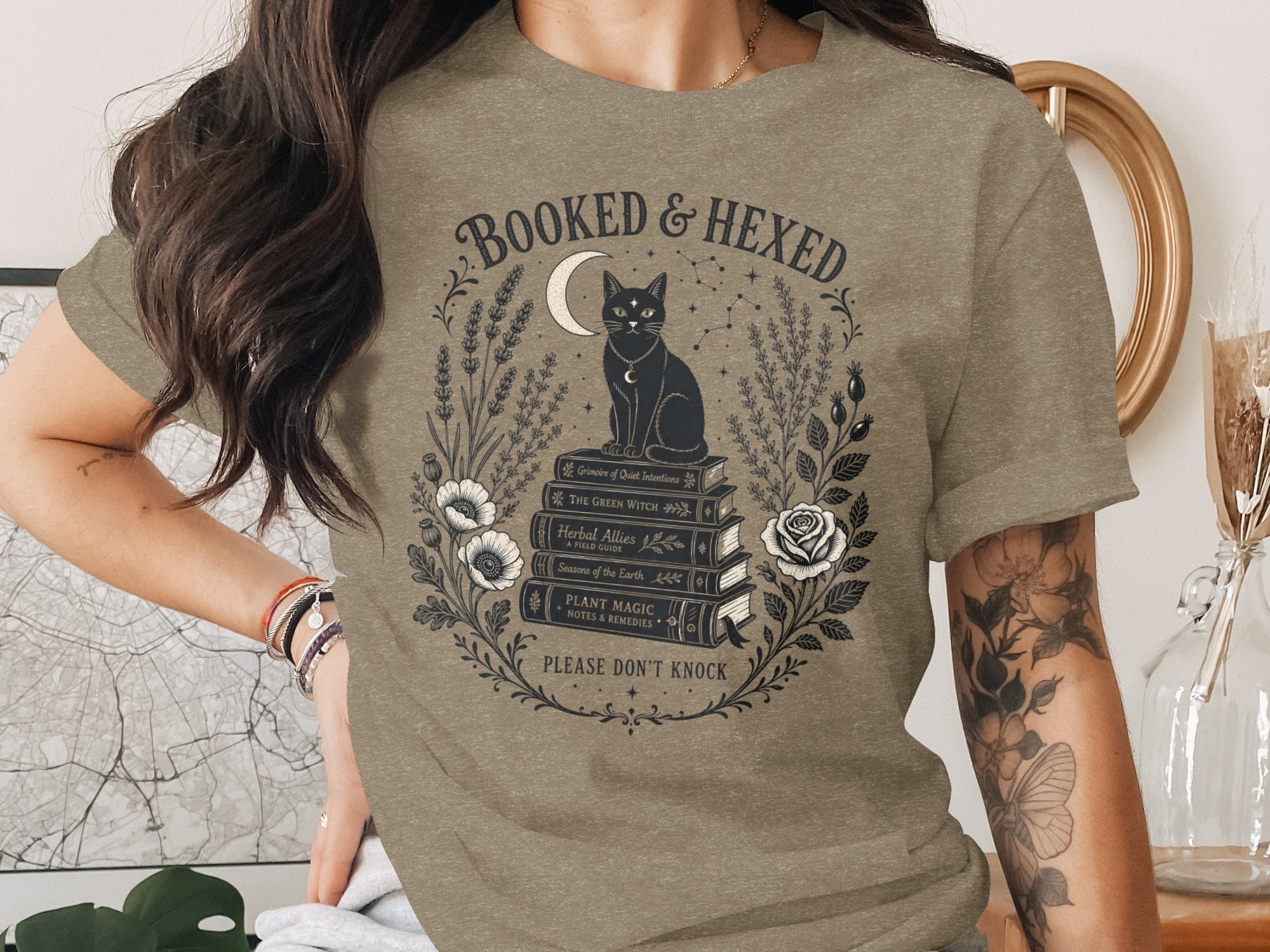 T-shirt with "Booked & Hexed" and black cat on books, surrounded by flora.