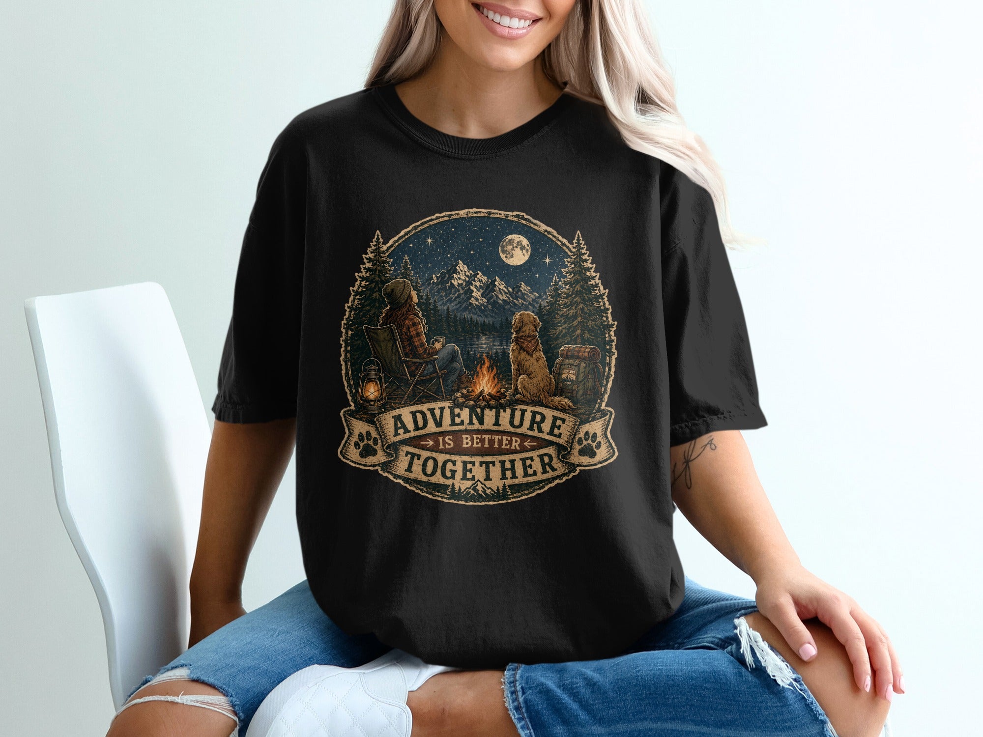 Black t-shirt graphic showing camping scene with a person, dog, campfire, and mountains. Text reads "Adventure is Better Together."