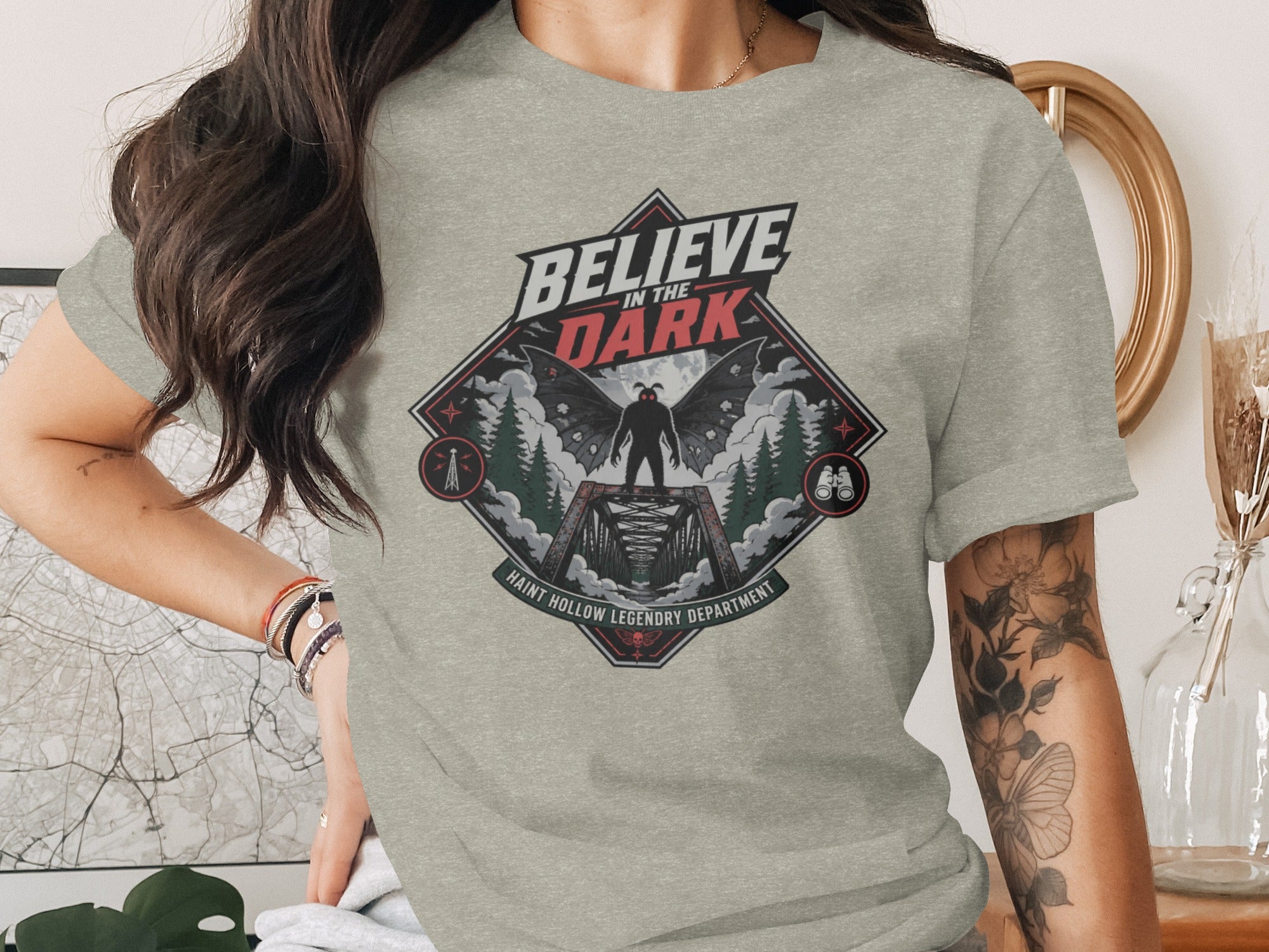 T-shirt graphic: "Believe in the Dark" with mothman on a bridge at night.