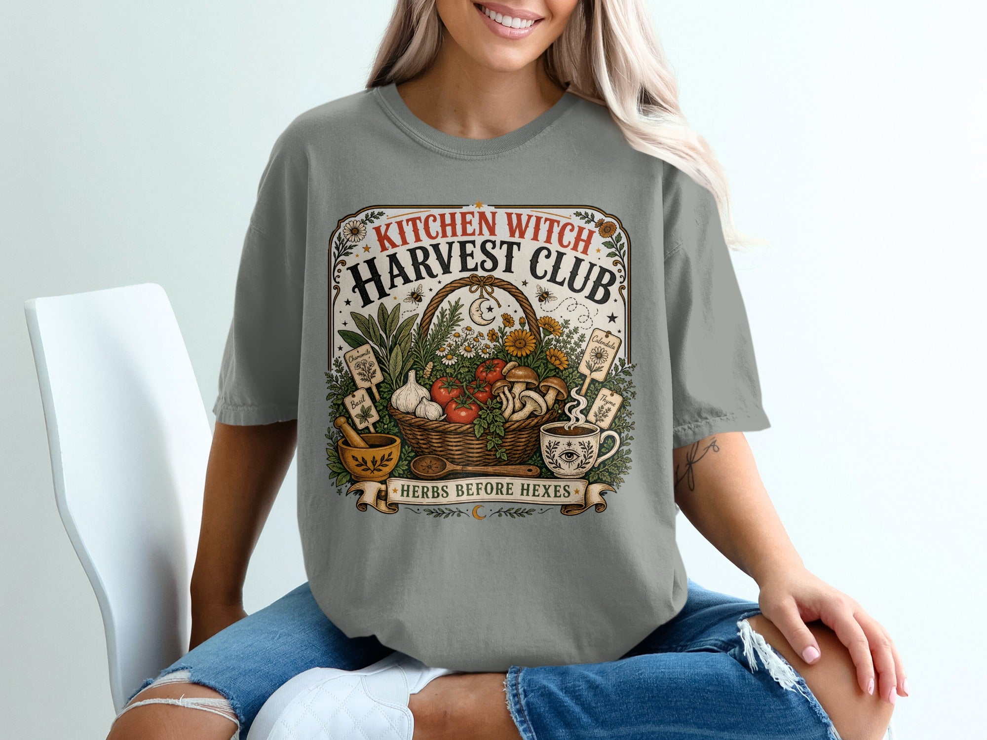 Grey t-shirt graphic: "KITCHEN WITCH HARVEST CLUB HERBS BEFORE HEXES" with basket of produce, mortar and pestle.