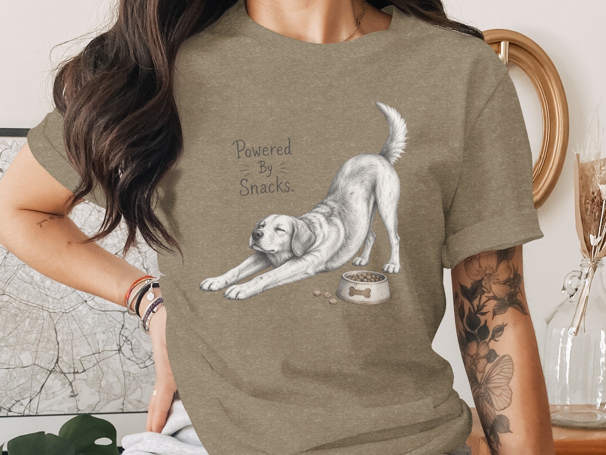 T-shirt graphic: White dog stretching next to food bowl, "Powered By Snacks." text.