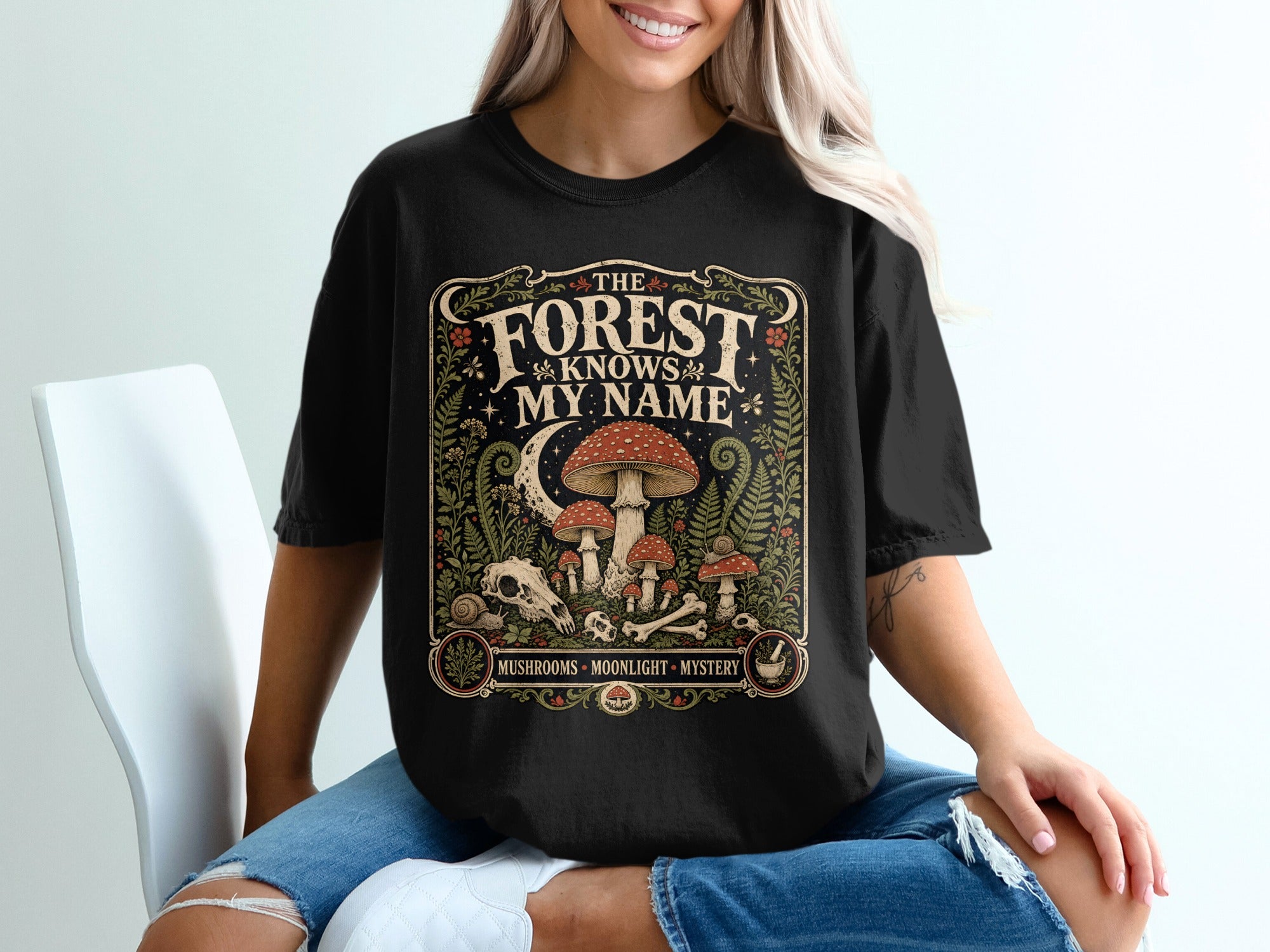 Black t-shirt with "The Forest Knows My Name" text and mushroom, moon, and bone design.