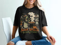 Black t-shirt graphic with a witch stirring a cauldron under the moon, text reads "SOUP, SPELLS & SOLITUDE".