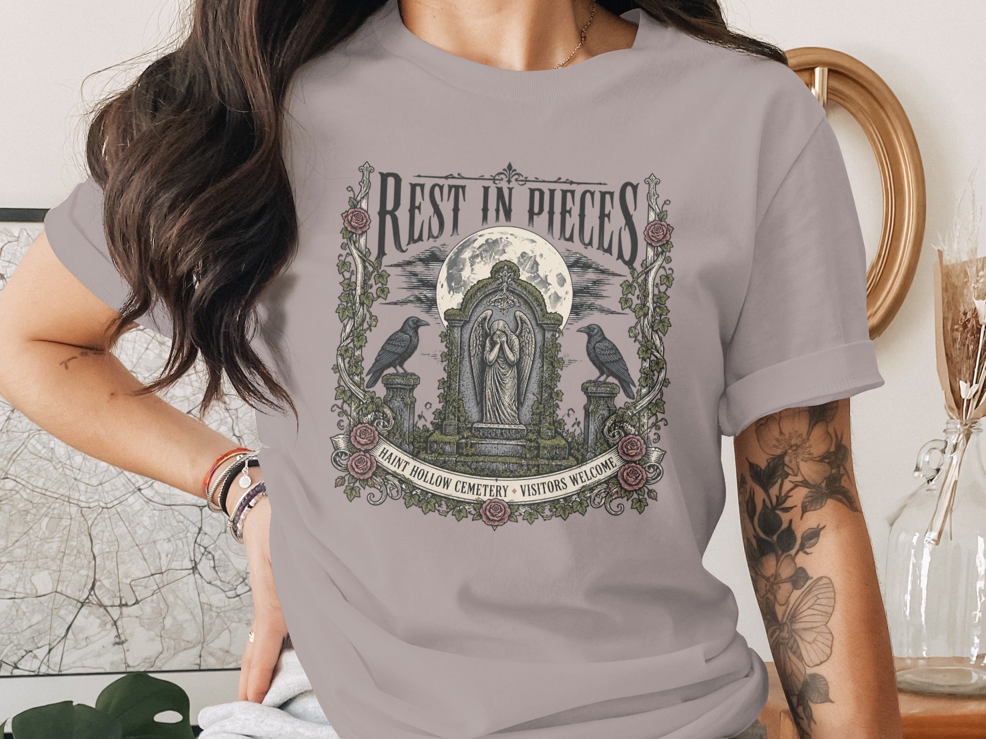 T-shirt graphic with "Rest in Pieces" text, cemetery, moon, angels, ravens, and roses.