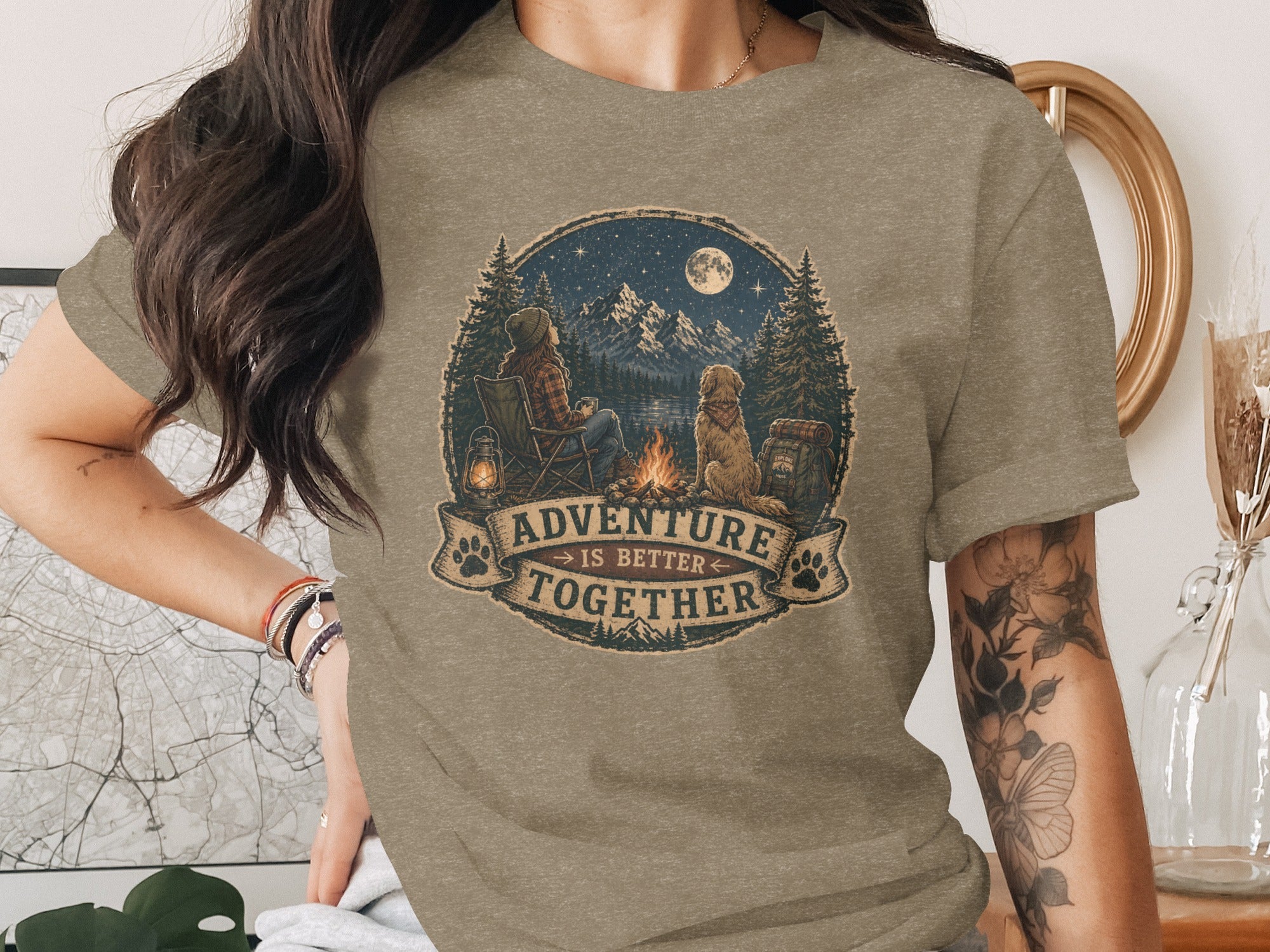 T-shirt graphic with woman, dog, campfire, mountains, moon, and text "Adventure Is Better Together".