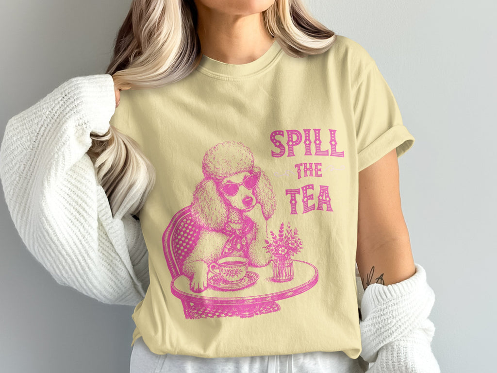 Yellow t-shirt with a pink graphic of a poodle wearing sunglasses, drinking tea. "SPILL THE TEA" text.