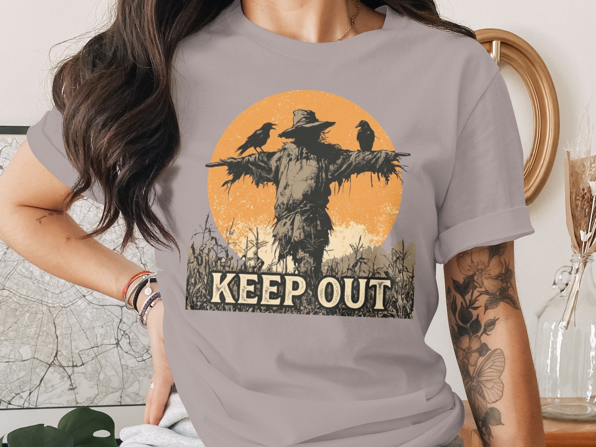 Scarecrow with crows in cornfield, text "KEEP OUT" on shirt.