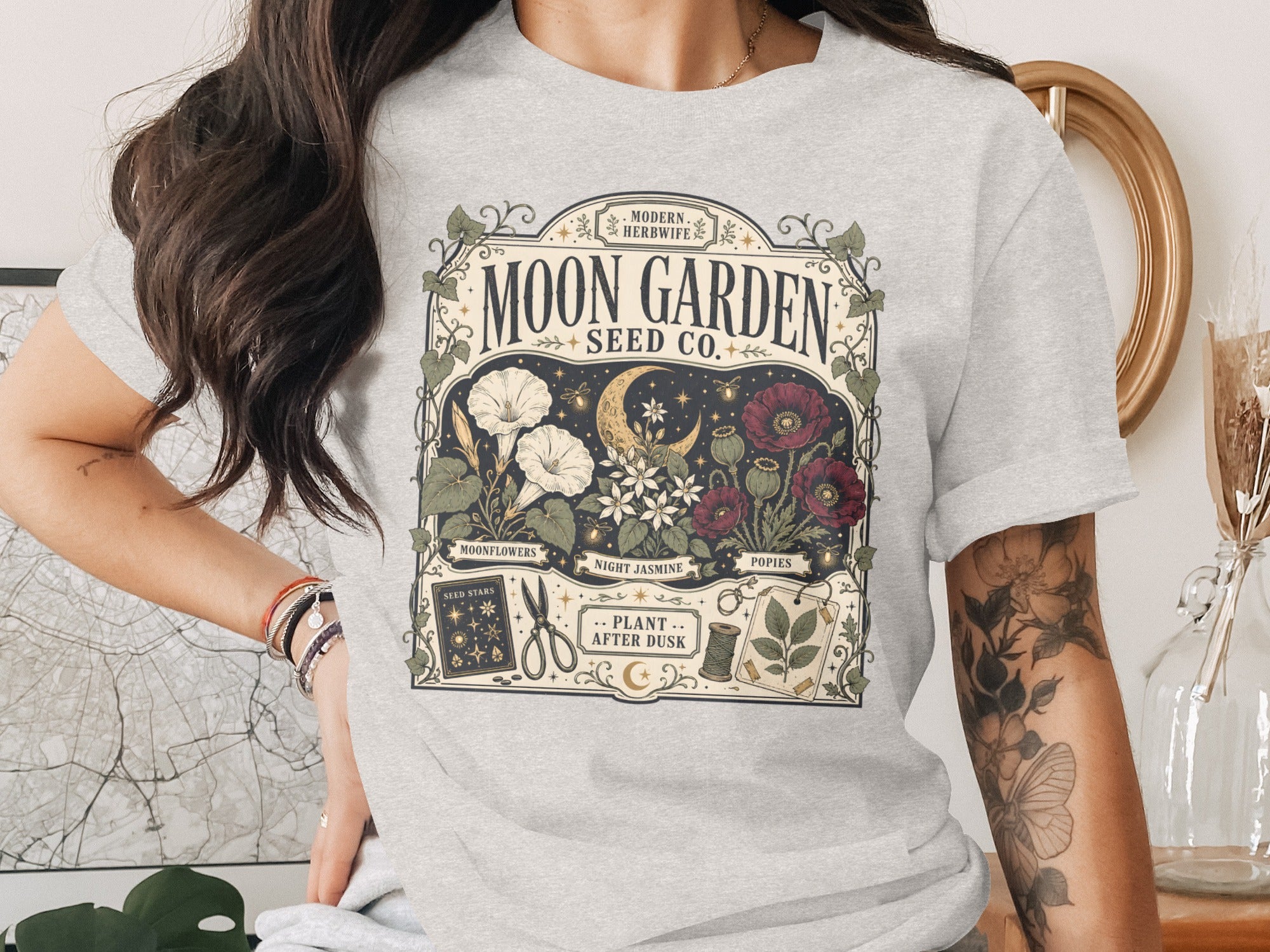 T-shirt with "Moon Garden Seed Co." design featuring moon, flowers, plants, and gardening tools.