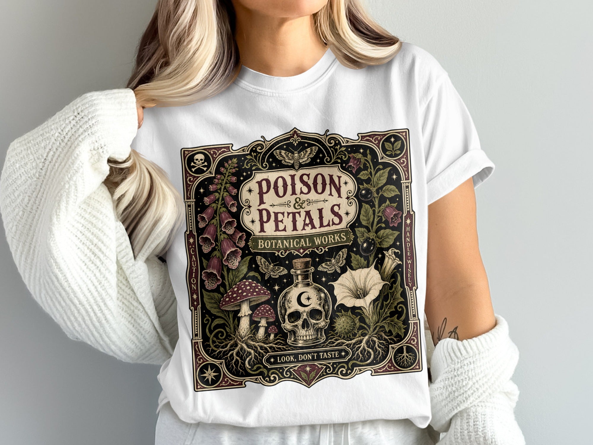 White t-shirt with "Poison Petals Botanical Works" design featuring skull, plants, and mushrooms.