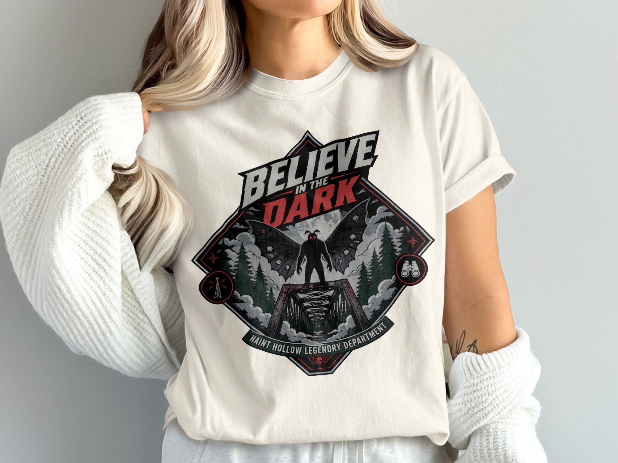 Believe in the Dark t-shirt featuring Mothman on a bridge and "Haint Hollow Legendry Department" text.
