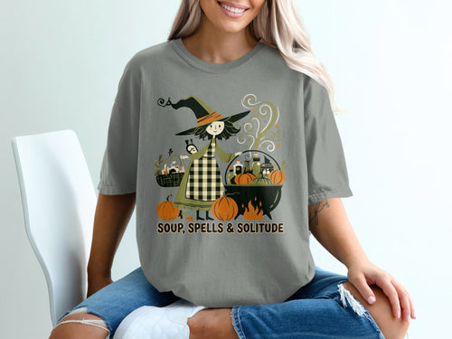 T-shirt graphic of a witch with pumpkins, cauldron, and text "SOUP, SPELLS & SOLITUDE".