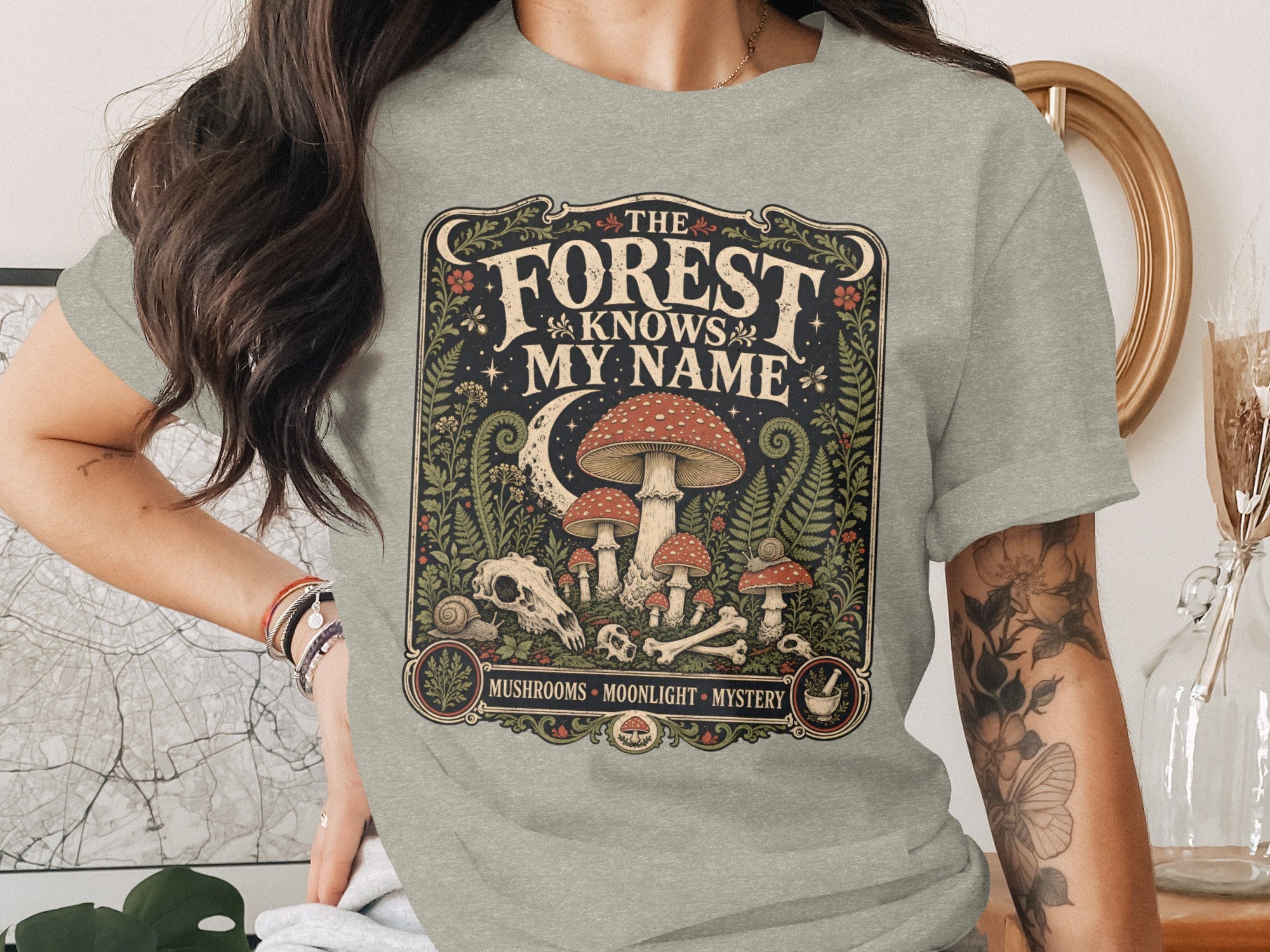 Grey t-shirt with "The Forest Knows My Name" design featuring mushrooms, skull, bones, and moon.