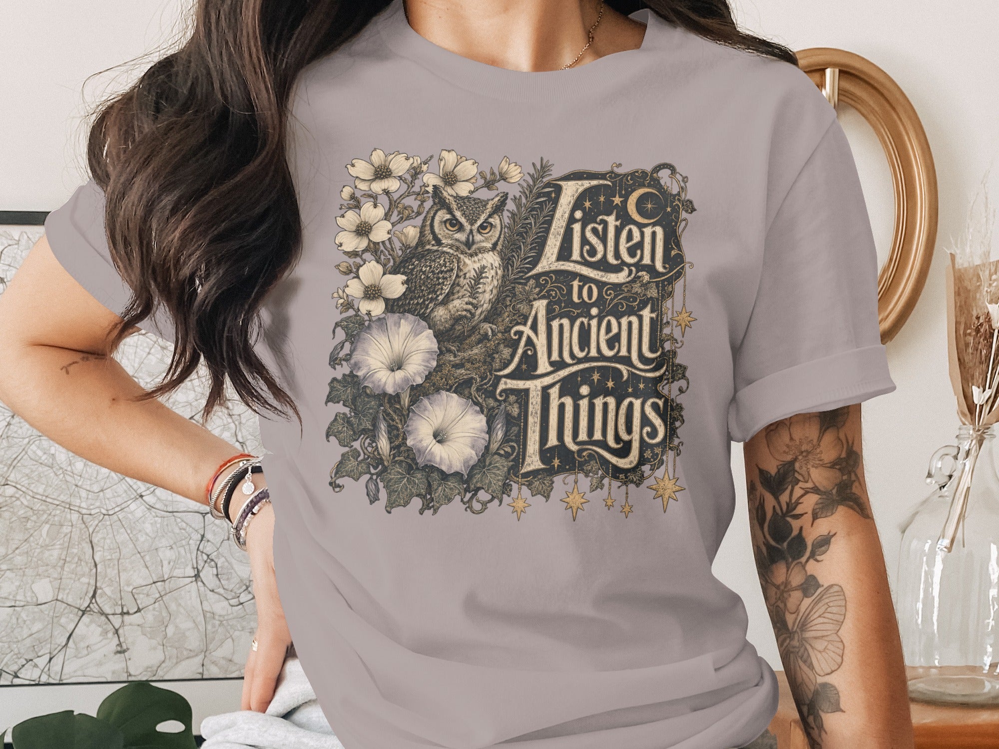 Graphic tee featuring an owl and flowers with "Listen to Ancient Things" text.