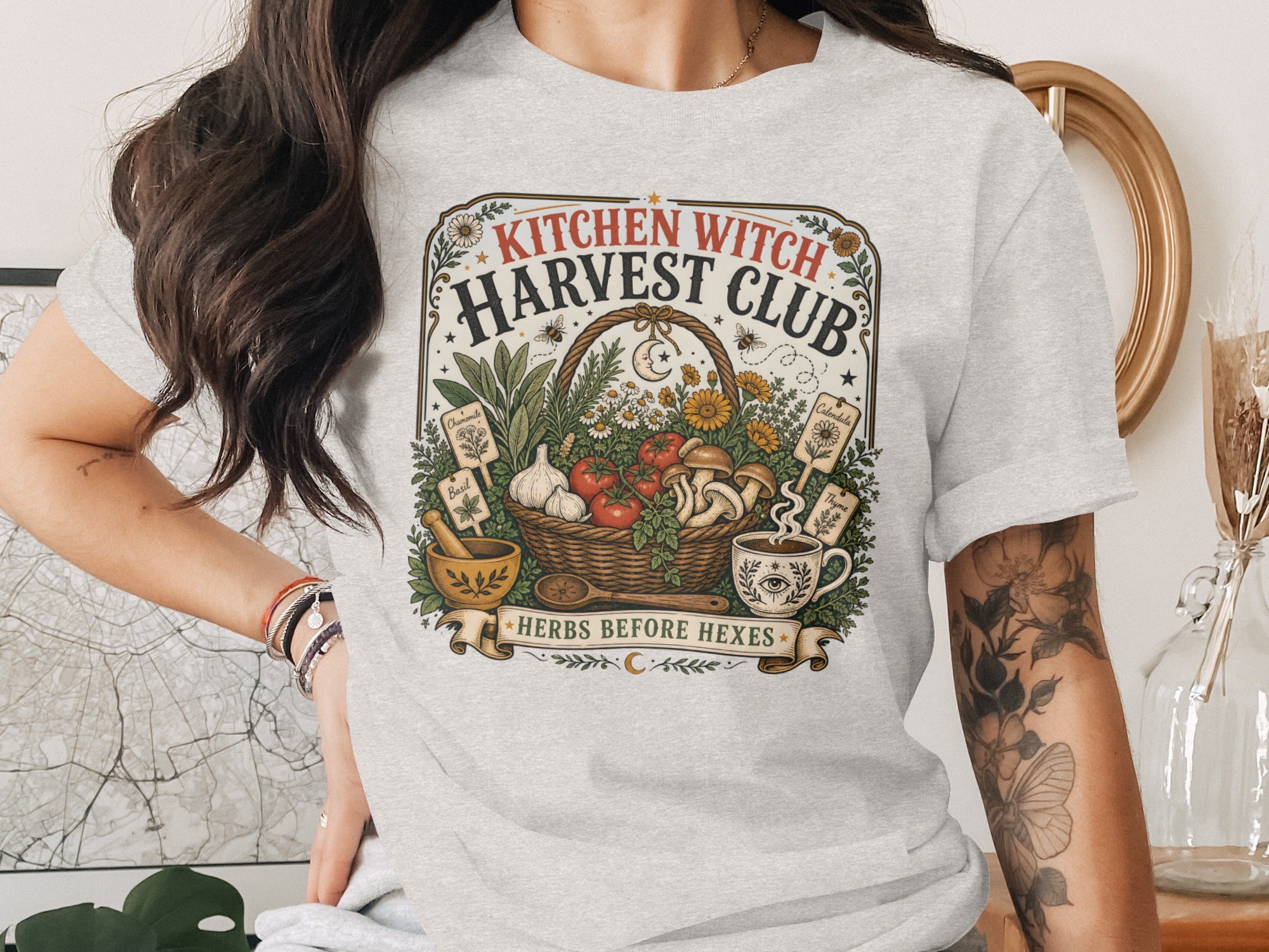 T-shirt graphic with "Kitchen Witch Harvest Club" and "Herbs Before Hexes" text.
