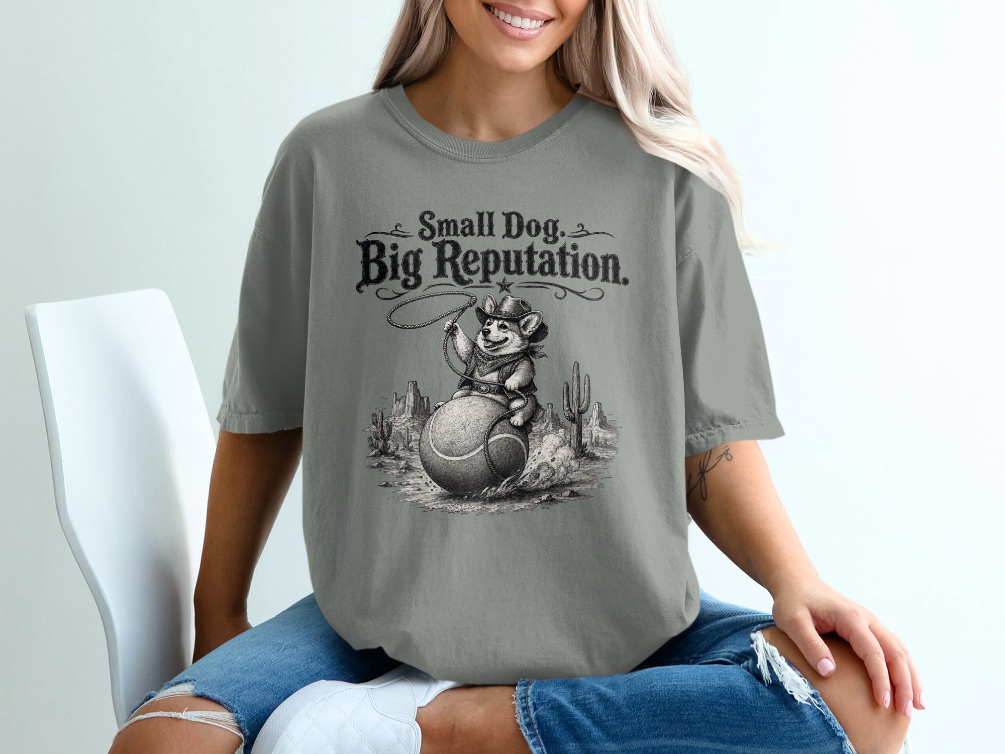 T-shirt graphic with "Small Dog. Big Reputation." text above a corgi cowboy riding a tennis ball.
