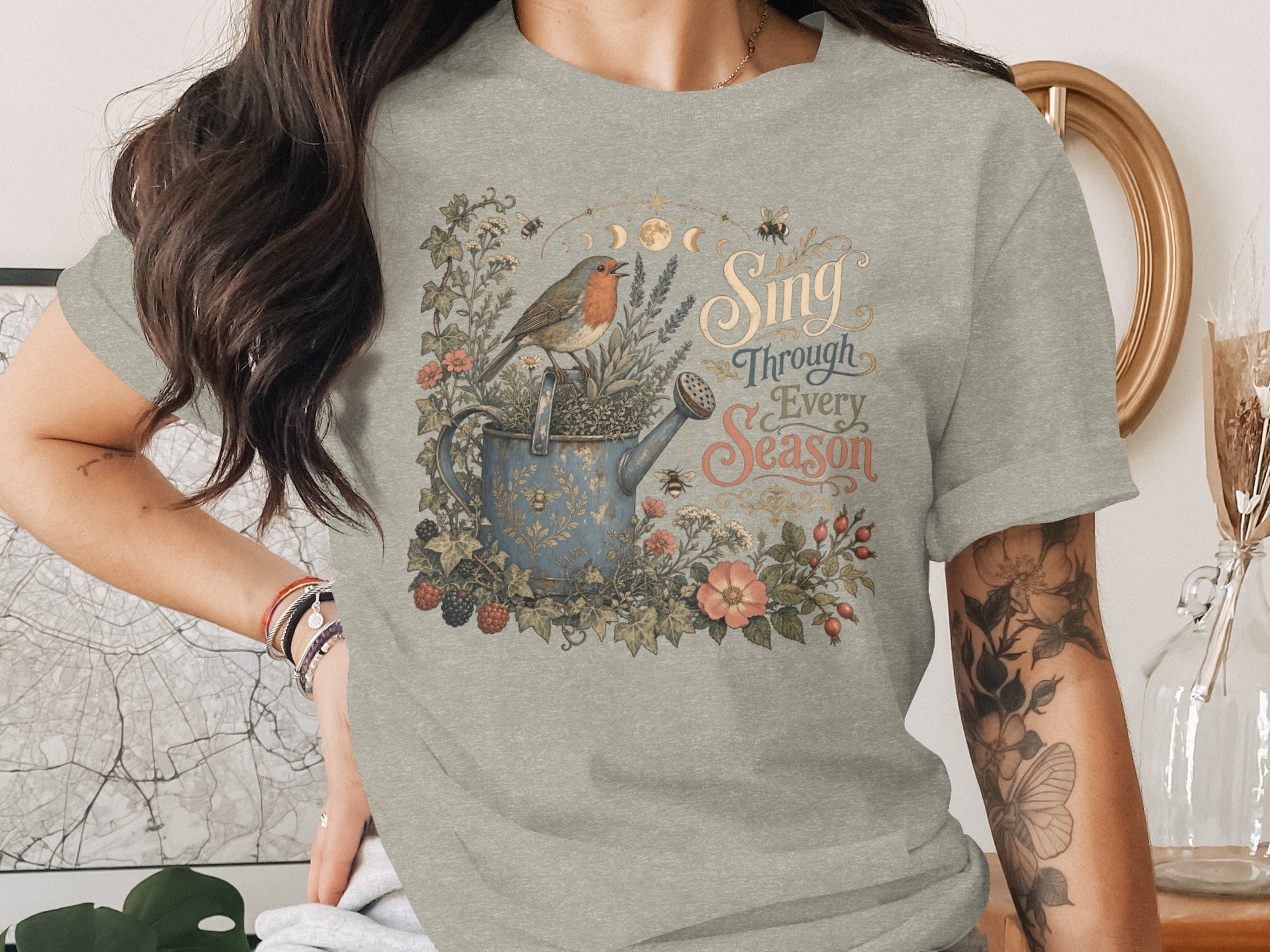 Robin on watering can with plants, bees, and text "Sing Through Every Season."