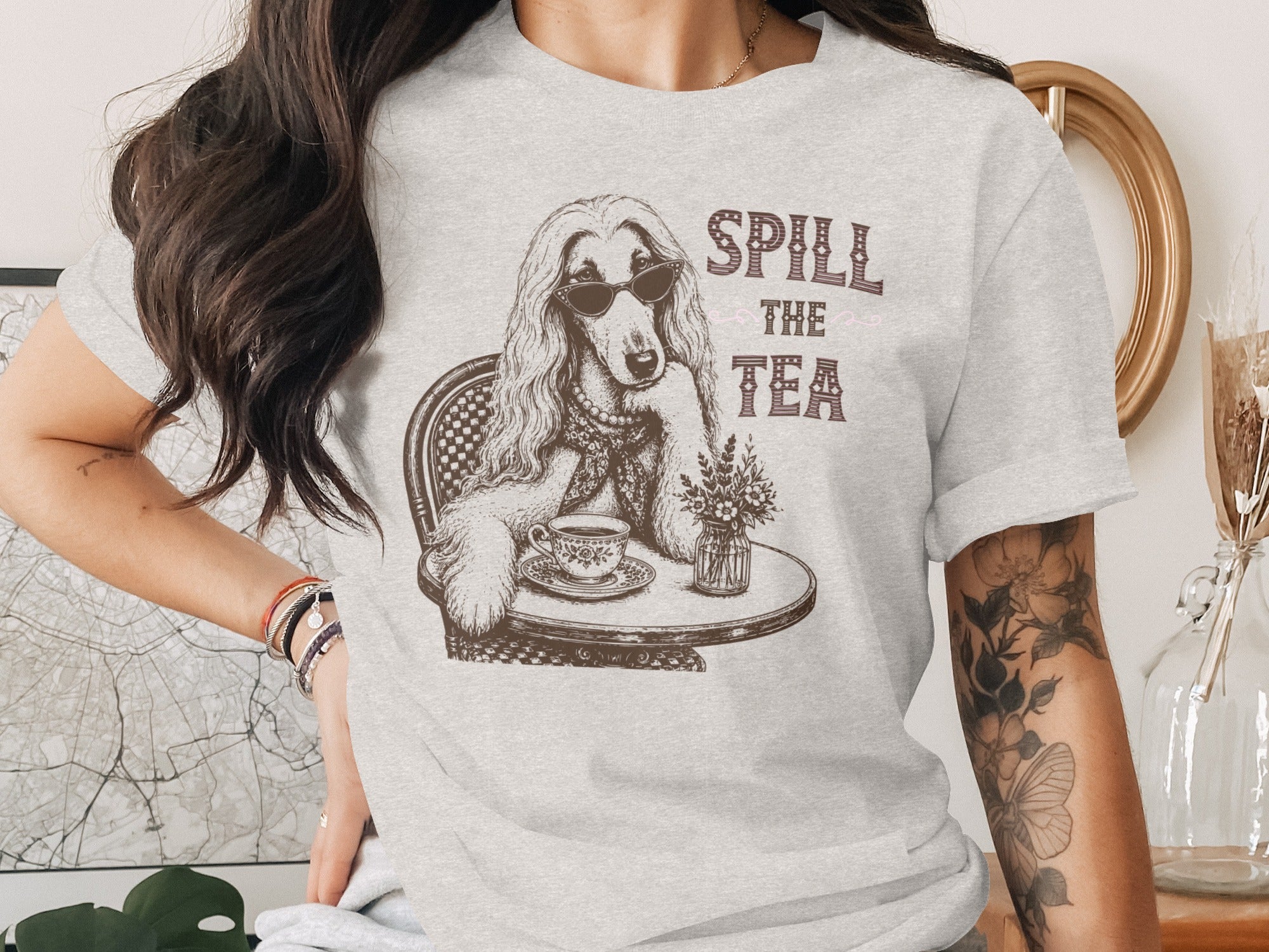 Afghan hound wearing sunglasses sits at a table with a cup of tea and text "SPill THE TEA".
