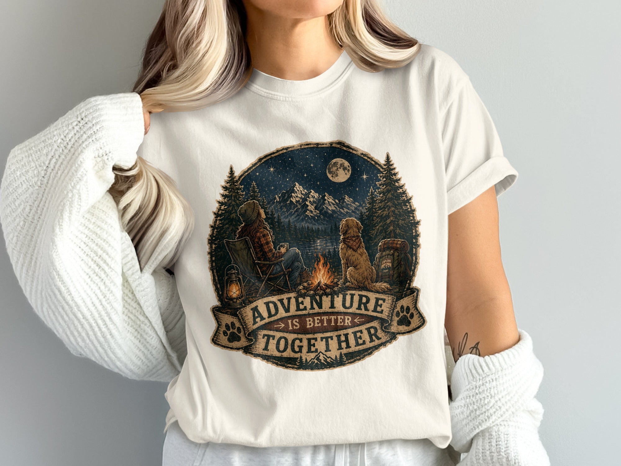 T-shirt graphic of person and dog by campfire with text "Adventure is Better Together".