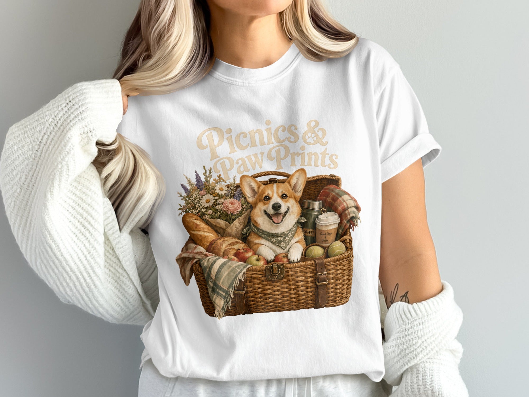 T-shirt graphic with text "Picnics & Paw Prints" above a corgi in a picnic basket.