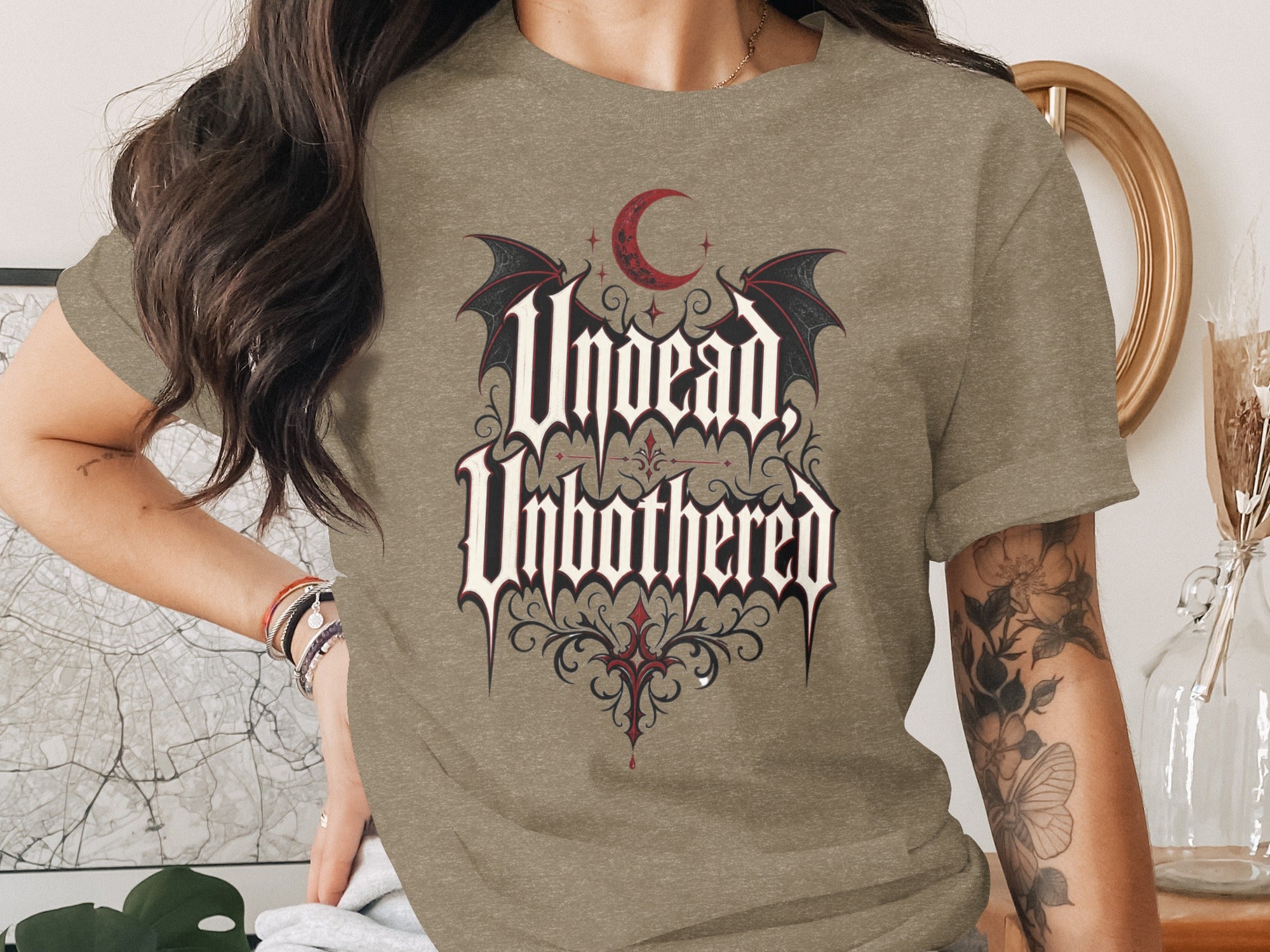 T-shirt with text "Undead Unbothered" in gothic font, red crescent moon, and bat wings.